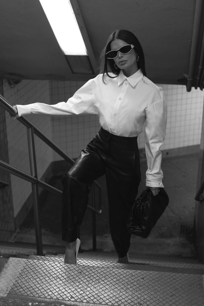 Victoria Barbara street style in New York City subway wearing white Bottega Veneta blouse top, Khaite black pants, black Bottega Veneta pouch handbag, white Balenciaga heeled shoes, & Loewe sunglasses during New York Fashion Week 2021