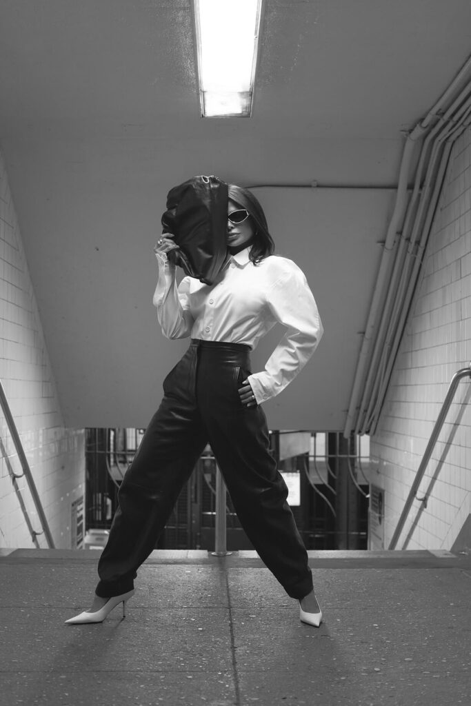 Victoria Barbara street style in New York City subway wearing white Bottega Veneta blouse top, Khaite black pants, black Bottega Veneta pouch handbag, white Balenciaga heeled shoes, & Loewe sunglasses during New York Fashion Week 2021