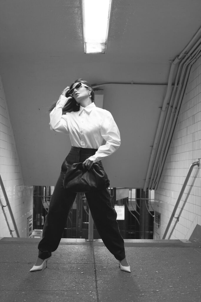 Victoria Barbara street style in New York City subway wearing white Bottega Veneta blouse top, Khaite black pants, black Bottega Veneta pouch handbag, white Balenciaga heeled shoes, & Loewe sunglasses during New York Fashion Week 2021