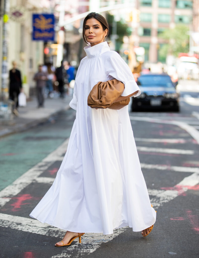 Victoria Barbara standing on a New York street in a white The Row dress paired with Bottega Veneta accessories during New York Fashion Week.