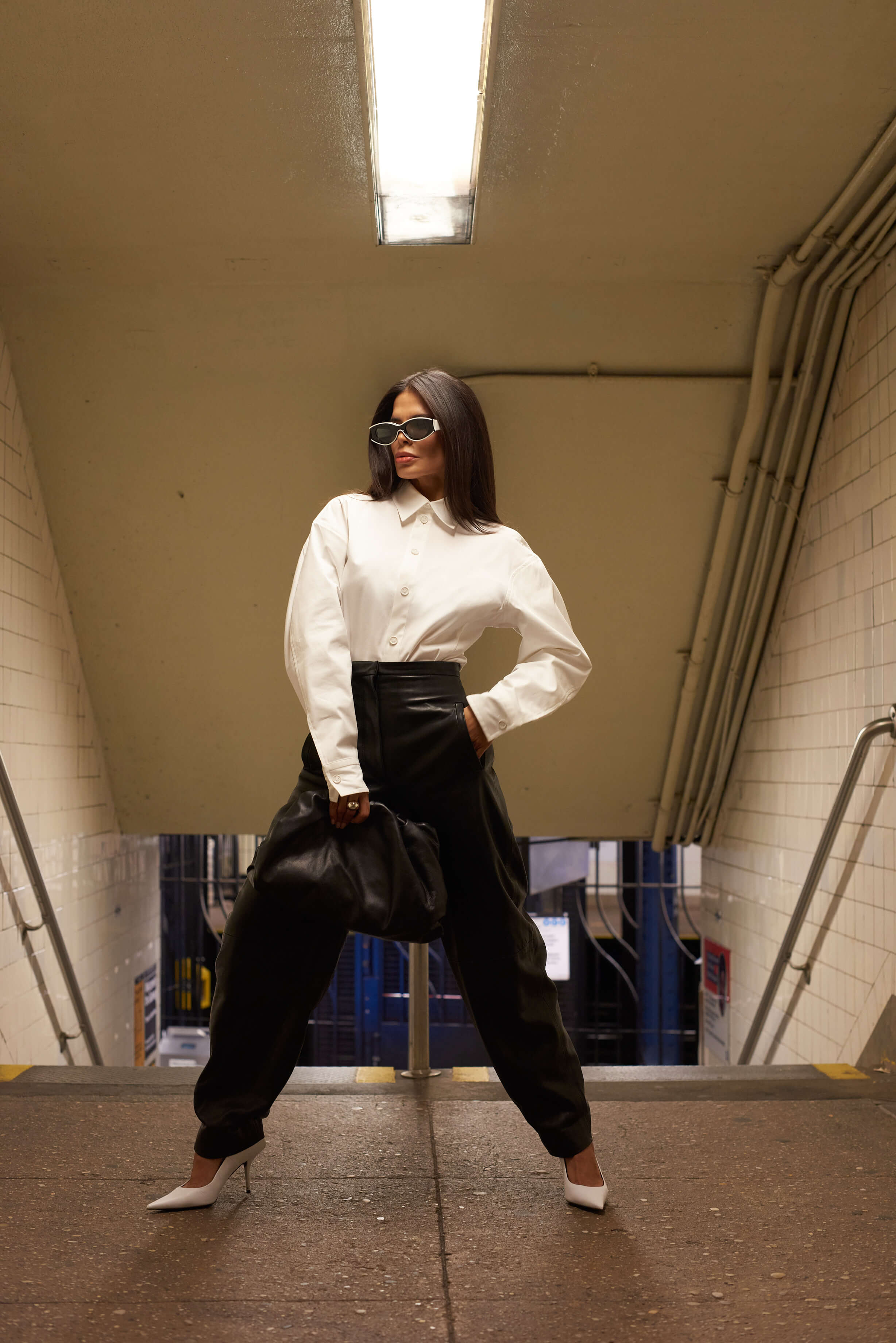 Victoria Barbara street style in New York City subway wearing white Bottega Veneta blouse top, Khaite black pants, black Bottega Veneta pouch handbag, white Balenciaga heeled shoes, & Loewe sunglasses during New York Fashion Week 2021