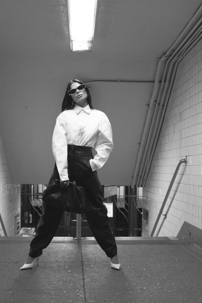 Victoria Barbara street style in New York City subway wearing white Bottega Veneta blouse top, Khaite black pants, black Bottega Veneta pouch handbag, white Balenciaga heeled shoes, & Loewe sunglasses during New York Fashion Week 2021