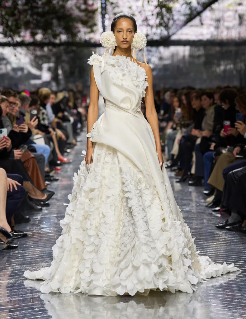 Model walking in Christian Dior Spring 2026 Couture ivory one-shoulder gown with floral appliqué and dramatic draped skirt