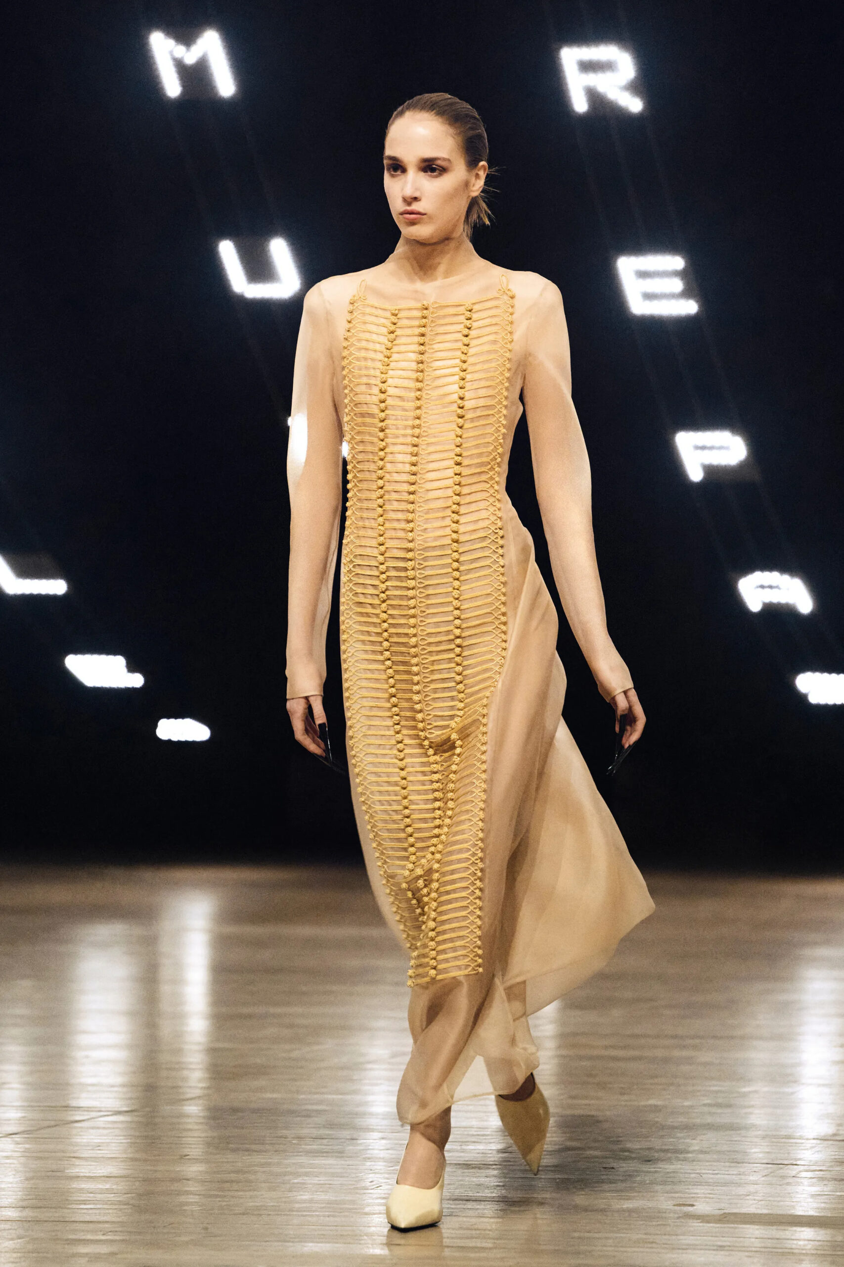 Model wearing a sheer nude dress with gold woven detailing at Khaite Fall Winter 2026 runway show