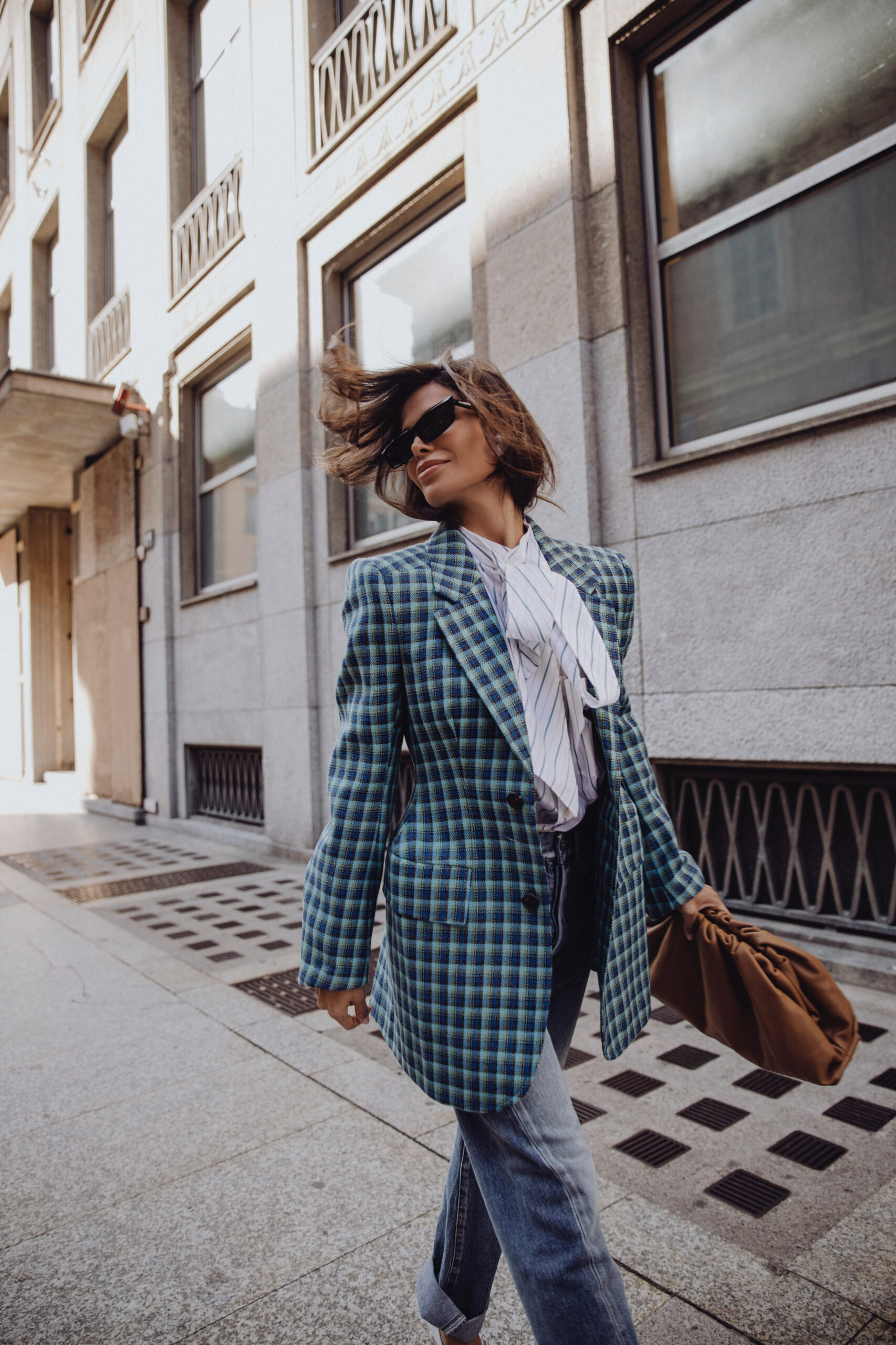 Woman in Balenciaga plaid blazer with wind movement and sunglasses outdoors