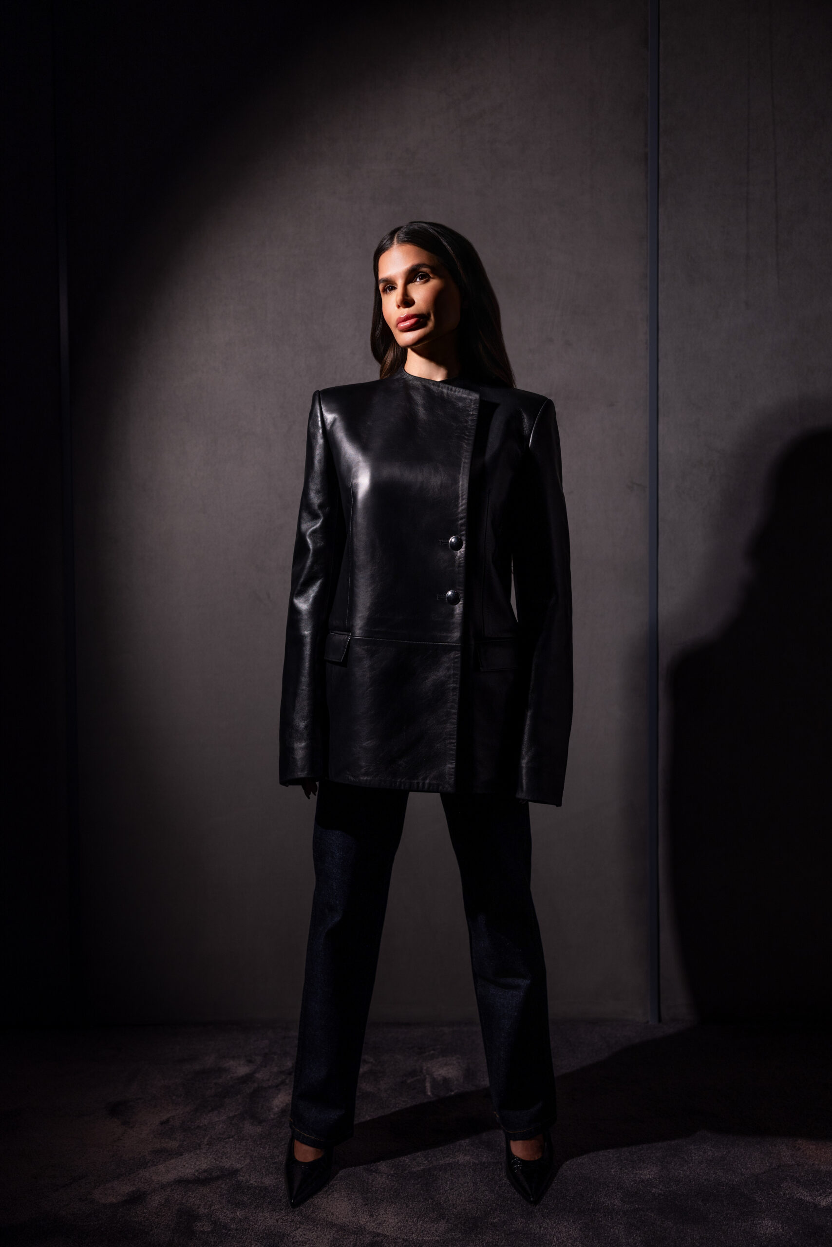 Victoria Barbara in Khaite black leather look in minimalist architectural interior with directional lighting
