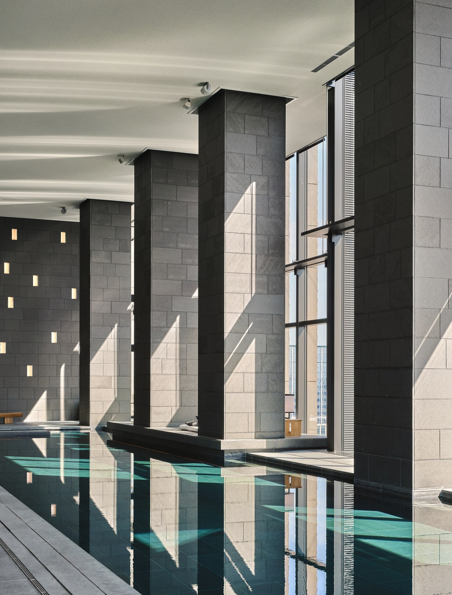 Aman Tokyo indoor pool with tall stone columns and reflective water creating a calm minimalist environment