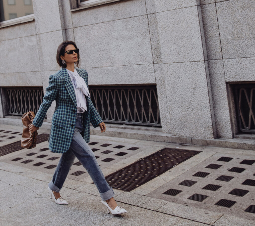 Woman wearing Balenciaga blazer with denim and heels walking in a city street