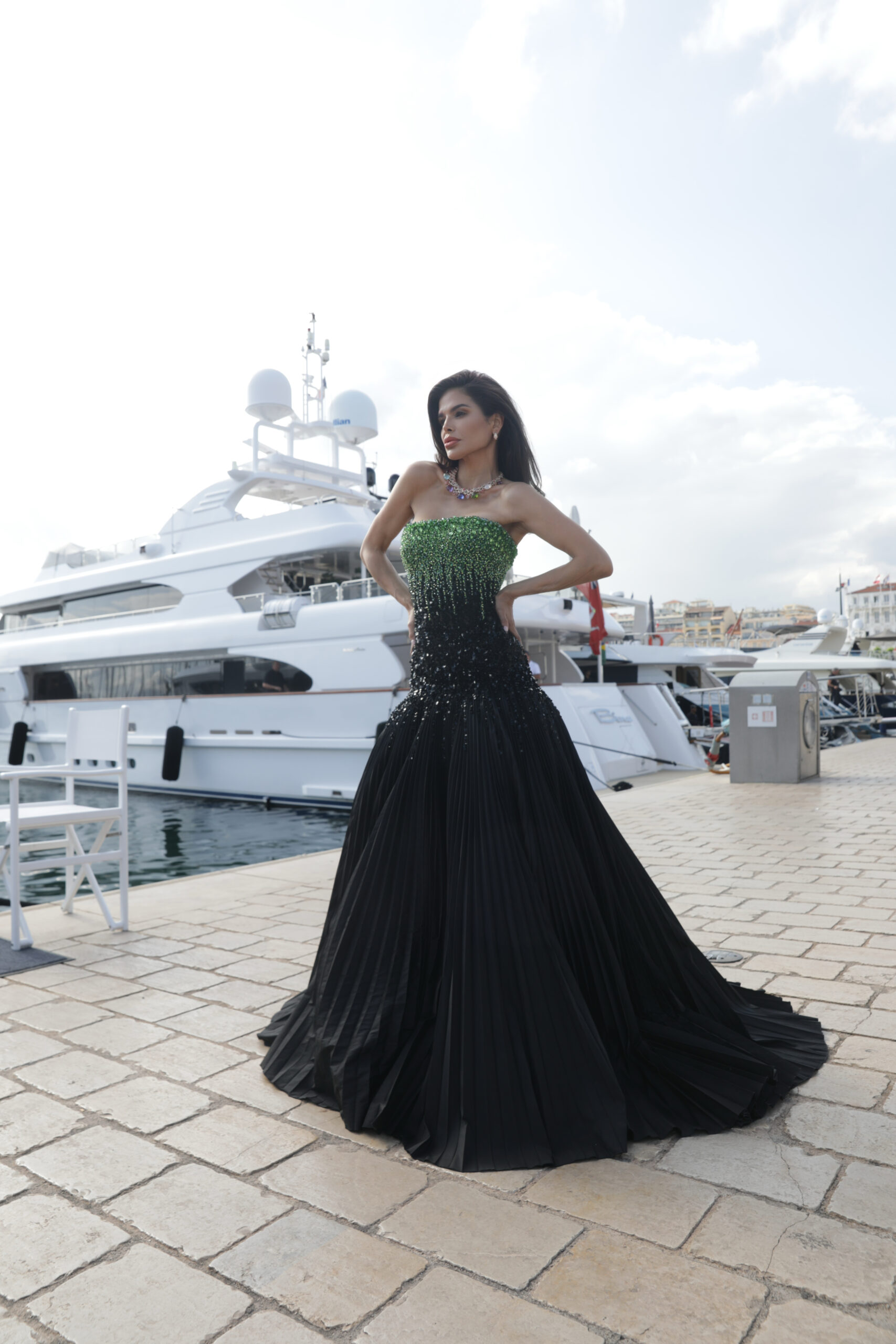 Victoria Barbara standing near yachts in Cannes harbor wearing a full-length Tony Ward Couture gown with green to black gradient design