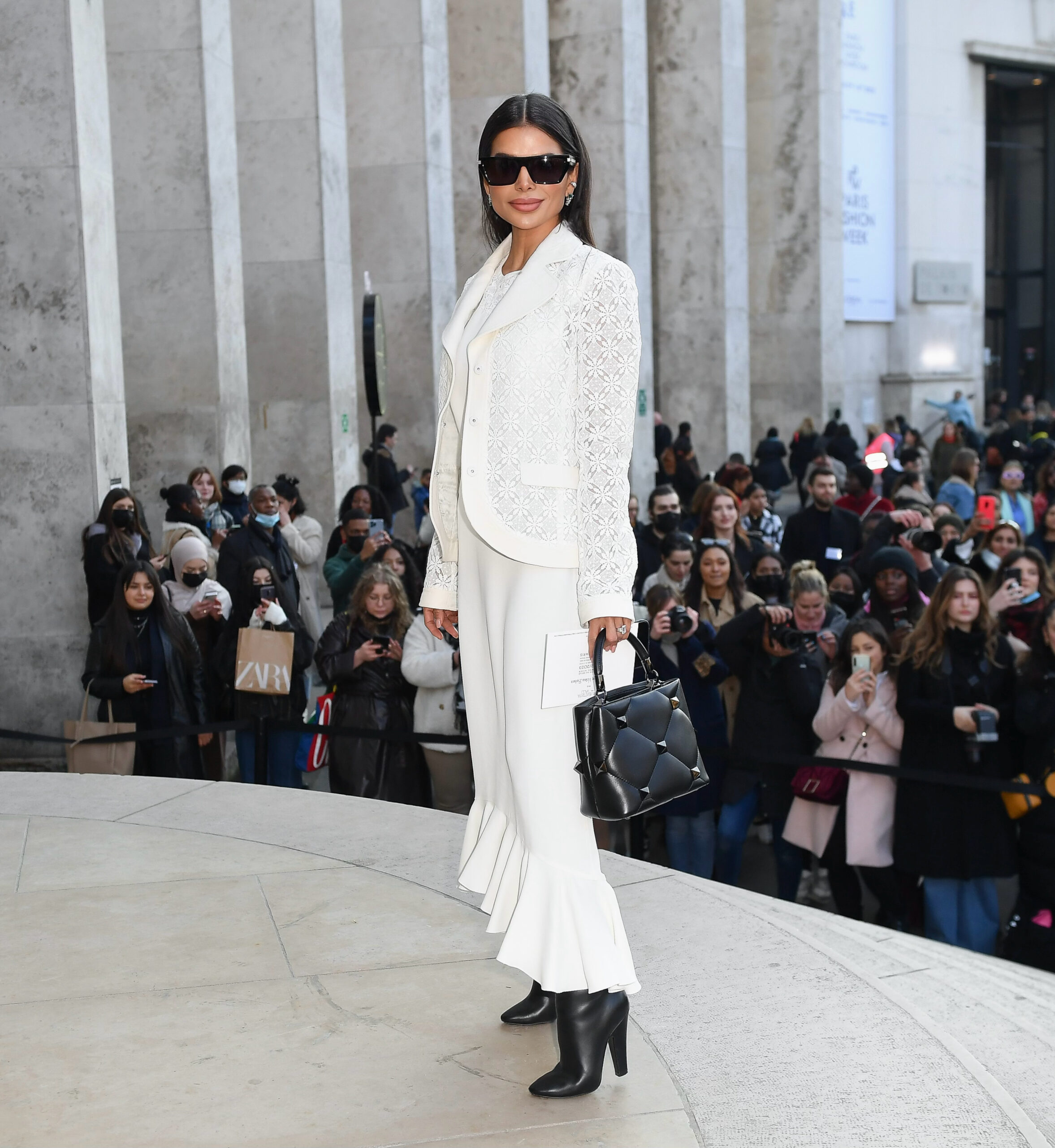 Victoria Barbara arriving at a Paris Couture Week show outside a venue, wearing a white tailored look, photographed among a crowd