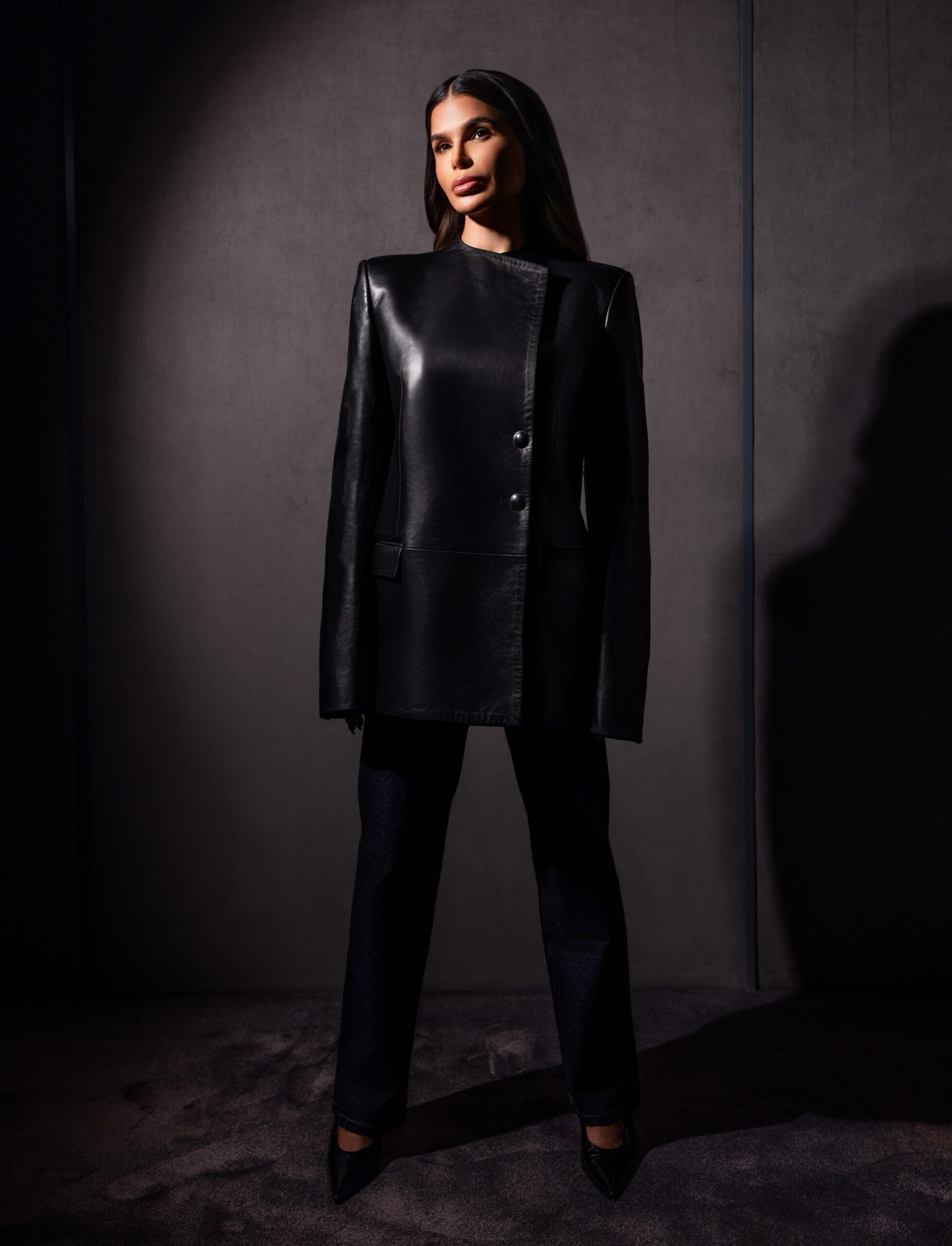 Khaite structured black leather blazer styled with straight-leg denim, strong front-facing editorial pose with sharp tailoring
