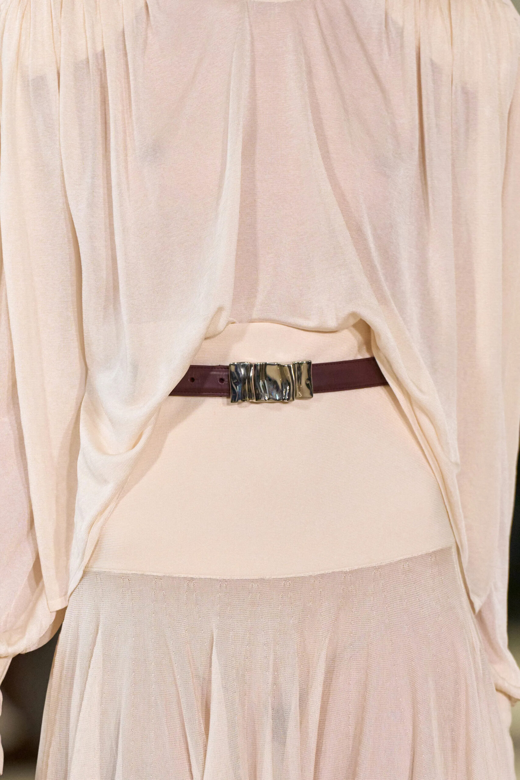 Close-up detail from the Altuzarra Fall Winter 2026 runway collection featuring a narrow black leather belt over soft ivory draped fabric at New York Fashion Week