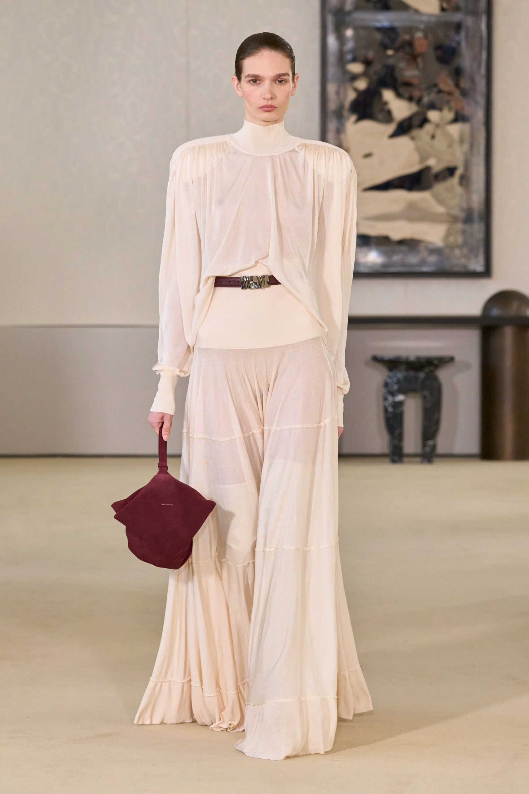 Model wearing a sheer cream layered dress with a burgundy handbag at Altuzarra Fall Winter 2026