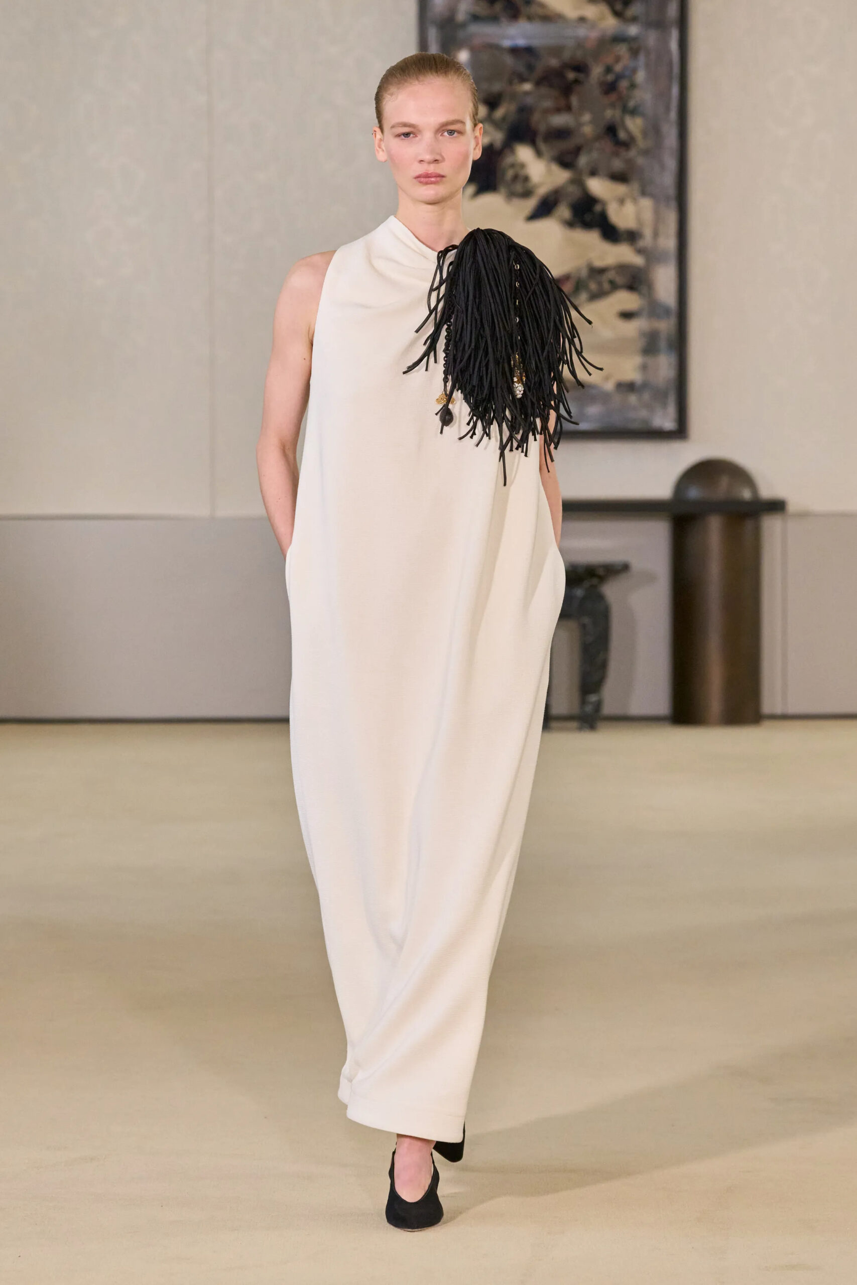 Model wearing an ivory column gown with black fringe shoulder detailing at Altuzarra Fall Winter 2026