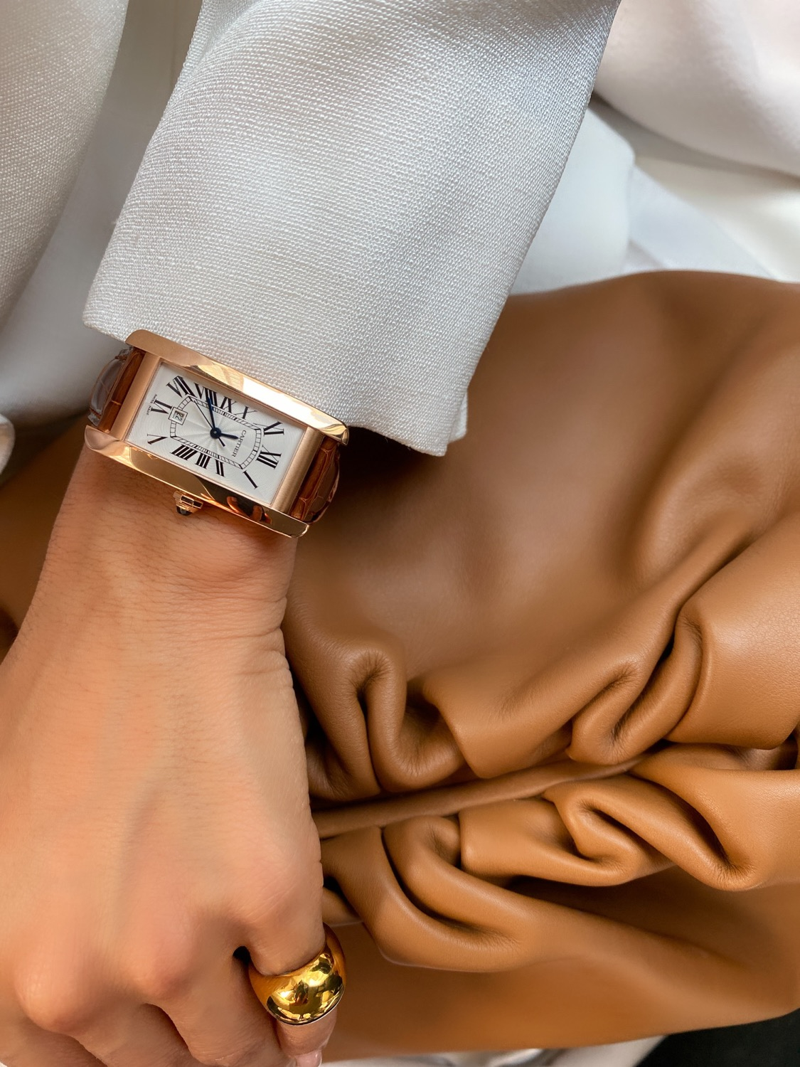 Close-up detail of a Cartier watch, gold ring, and Bottega Veneta leather clutch styled with Jil Sander tailoring.