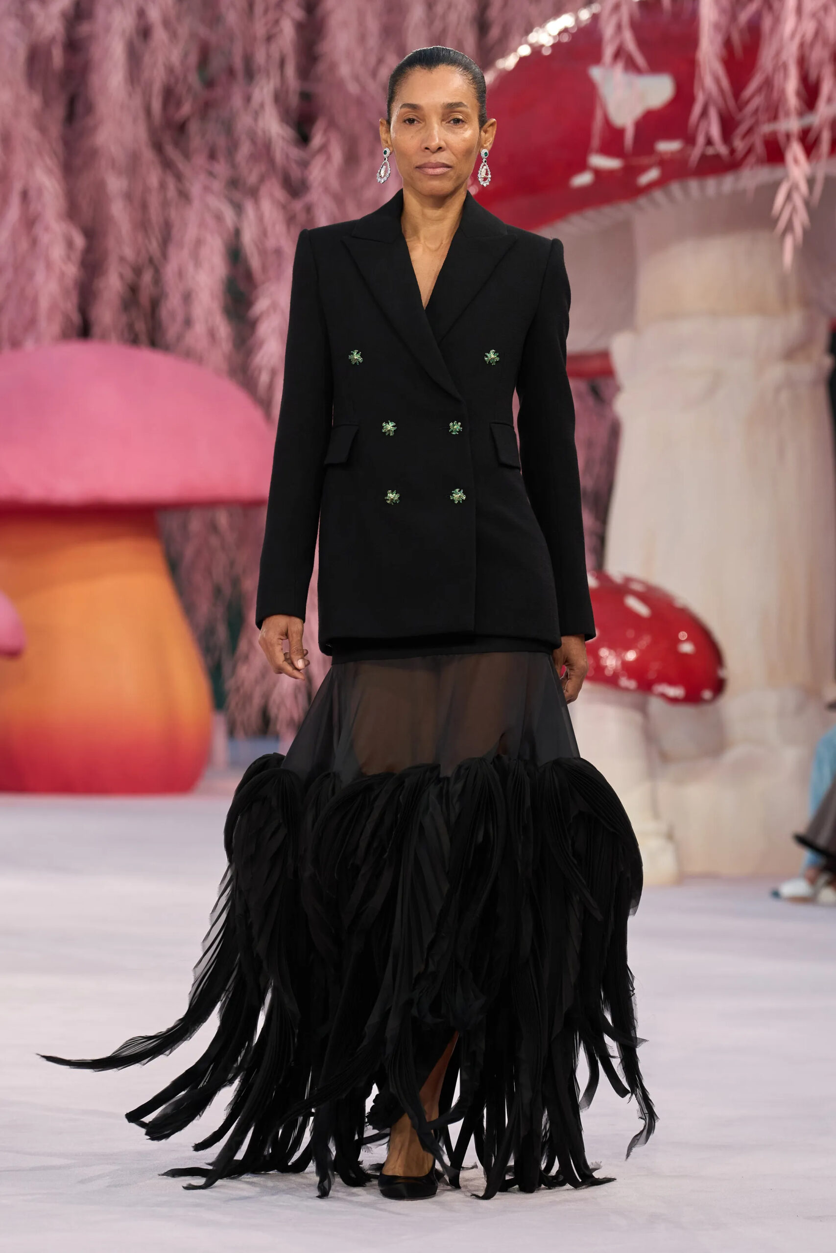 Model wearing a black tailored Chanel blazer with dramatic feathered skirt detail on the couture runway