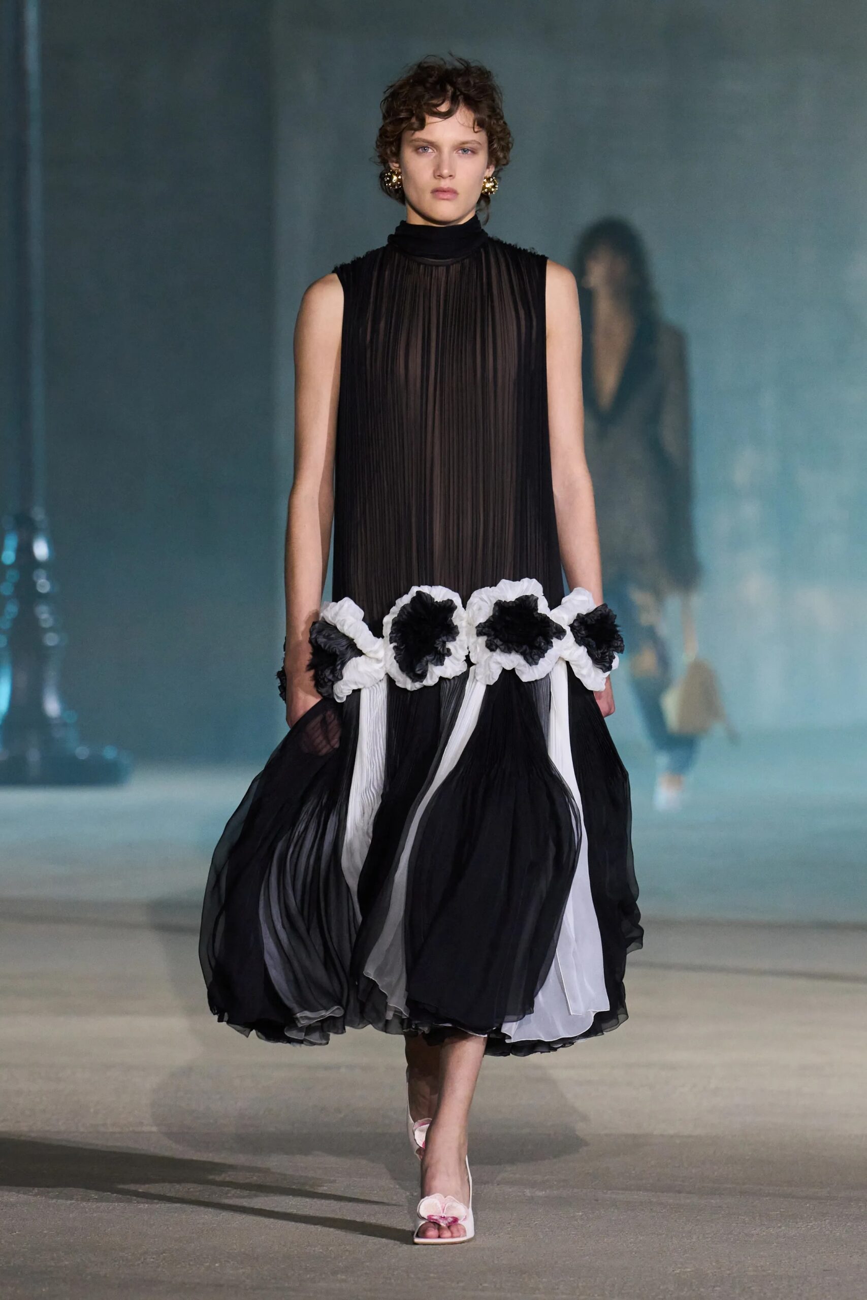 Black and white pleated Christian Dior Resort 2027 dress with oversized floral detailing at the waist and flowing sculptural skirt by Jonathan Anderson