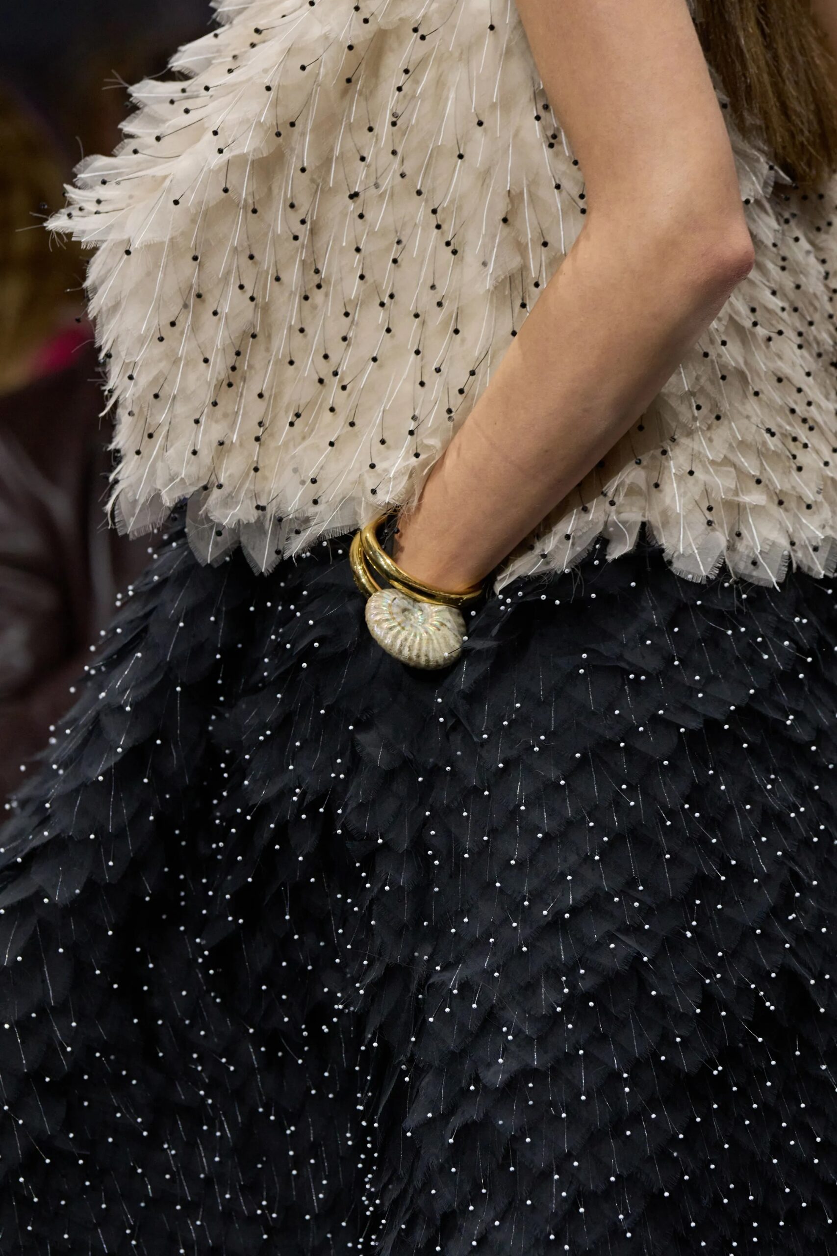 Close-up of Dior couture shell bracelet paired with feathered black and ivory fabric