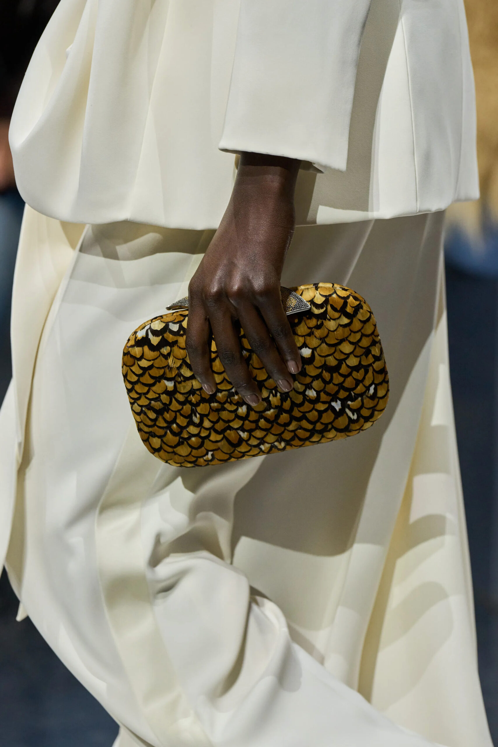 Close-up of gold textured Dior couture clutch carried with ivory draped gown