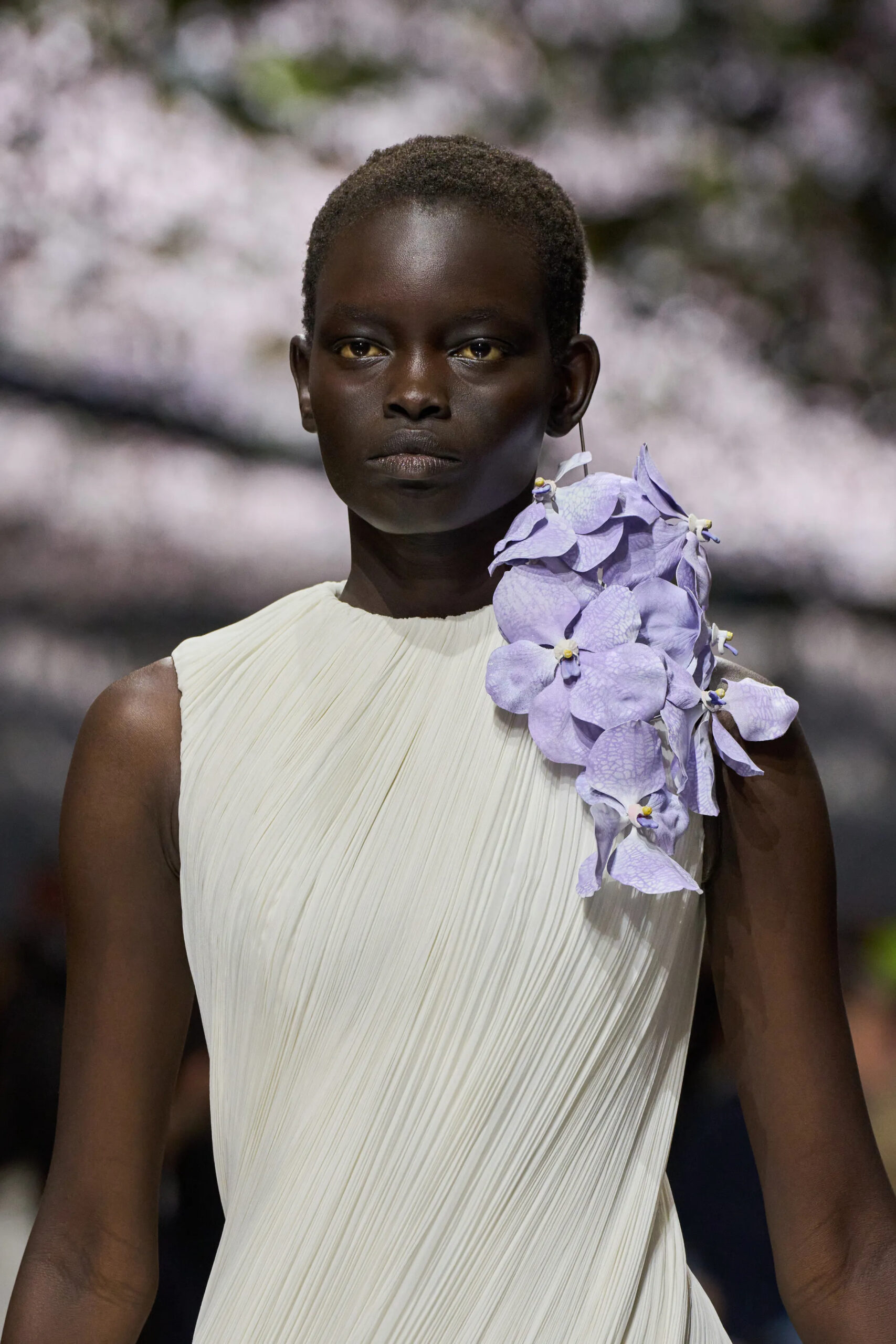 Close-up portrait of model wearing ivory pleated Dior couture gown with lavender orchid shoulder detail