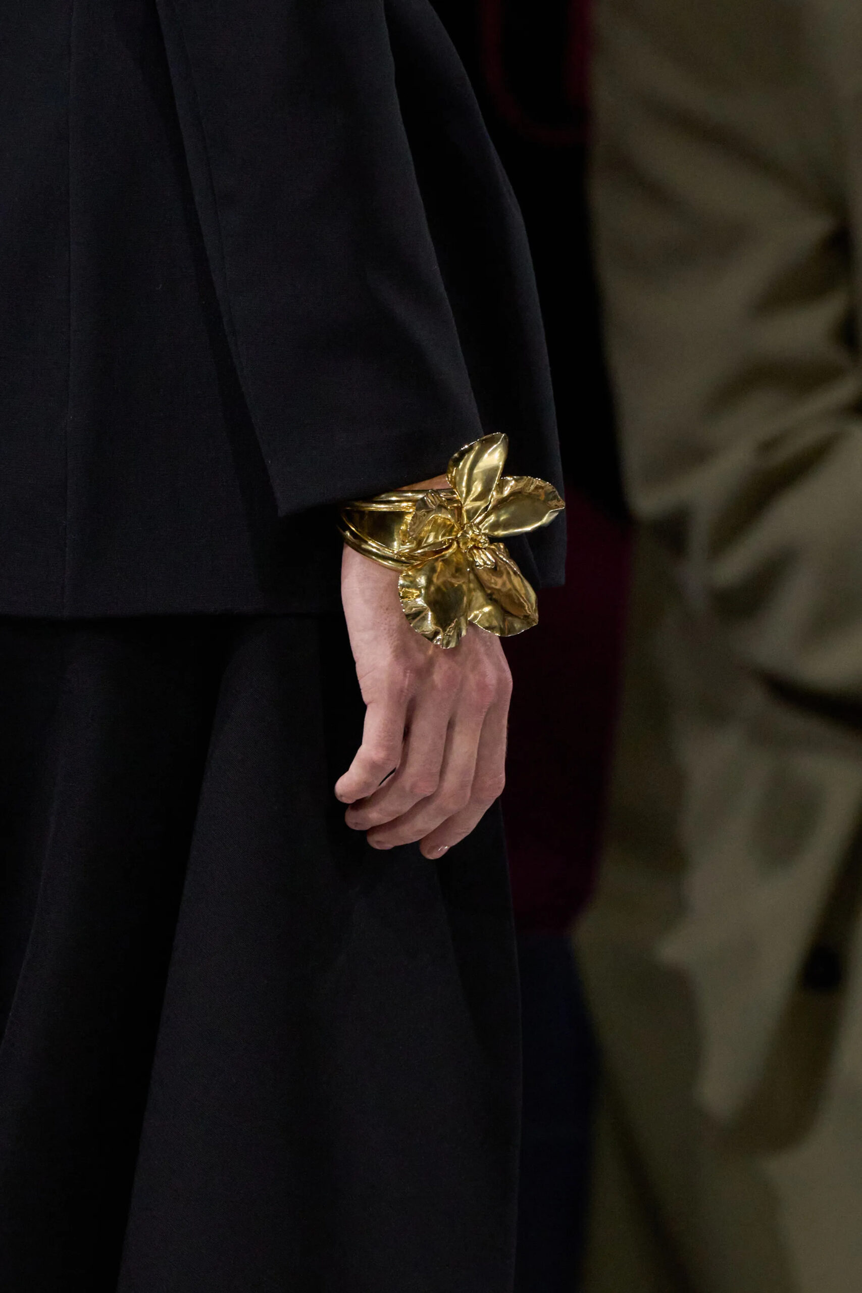 Close-up of gold floral Dior couture cuff bracelet worn with black tailoring