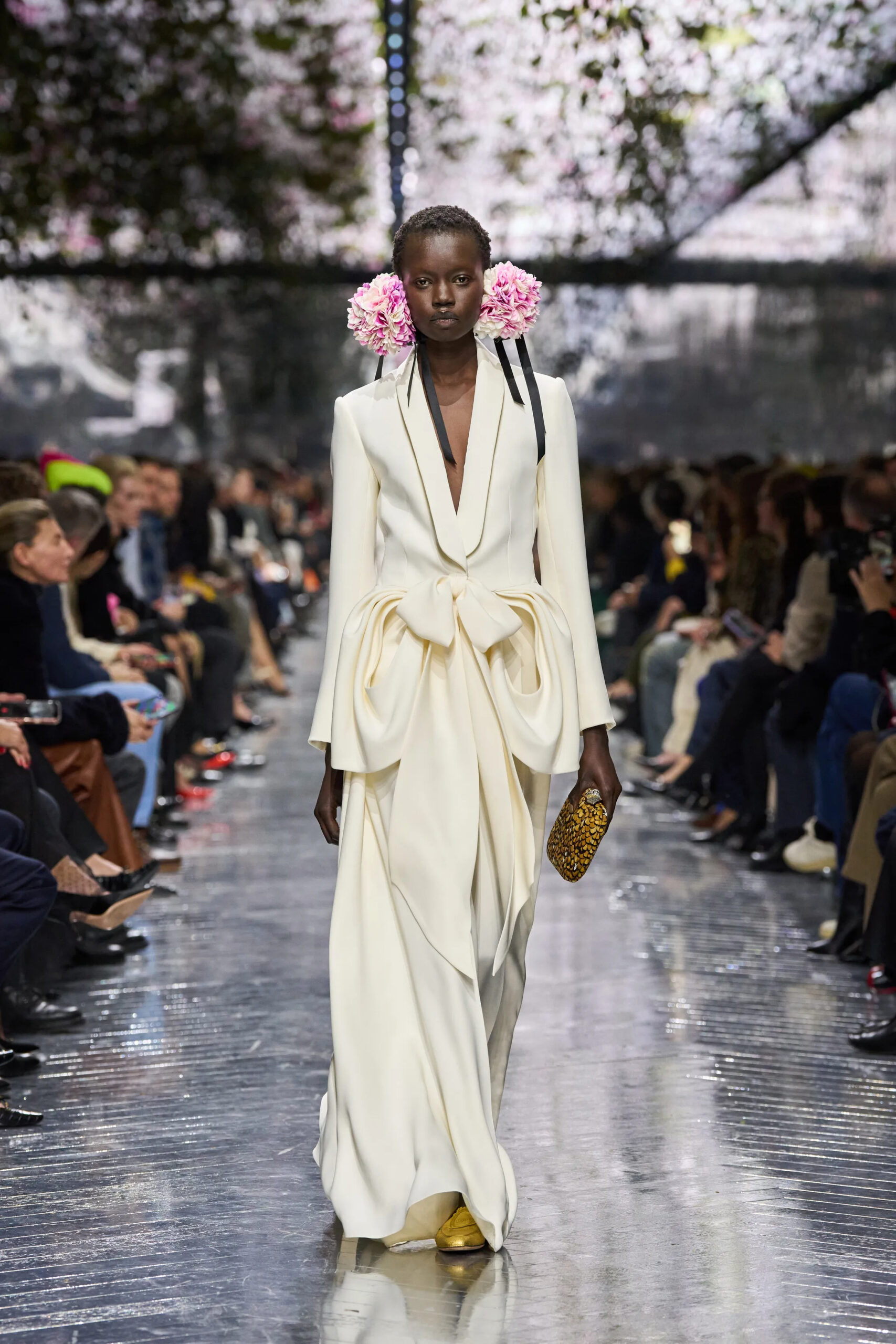 Model in ivory Christian Dior Spring 2026 Couture draped tailored gown carrying gold textured clutch