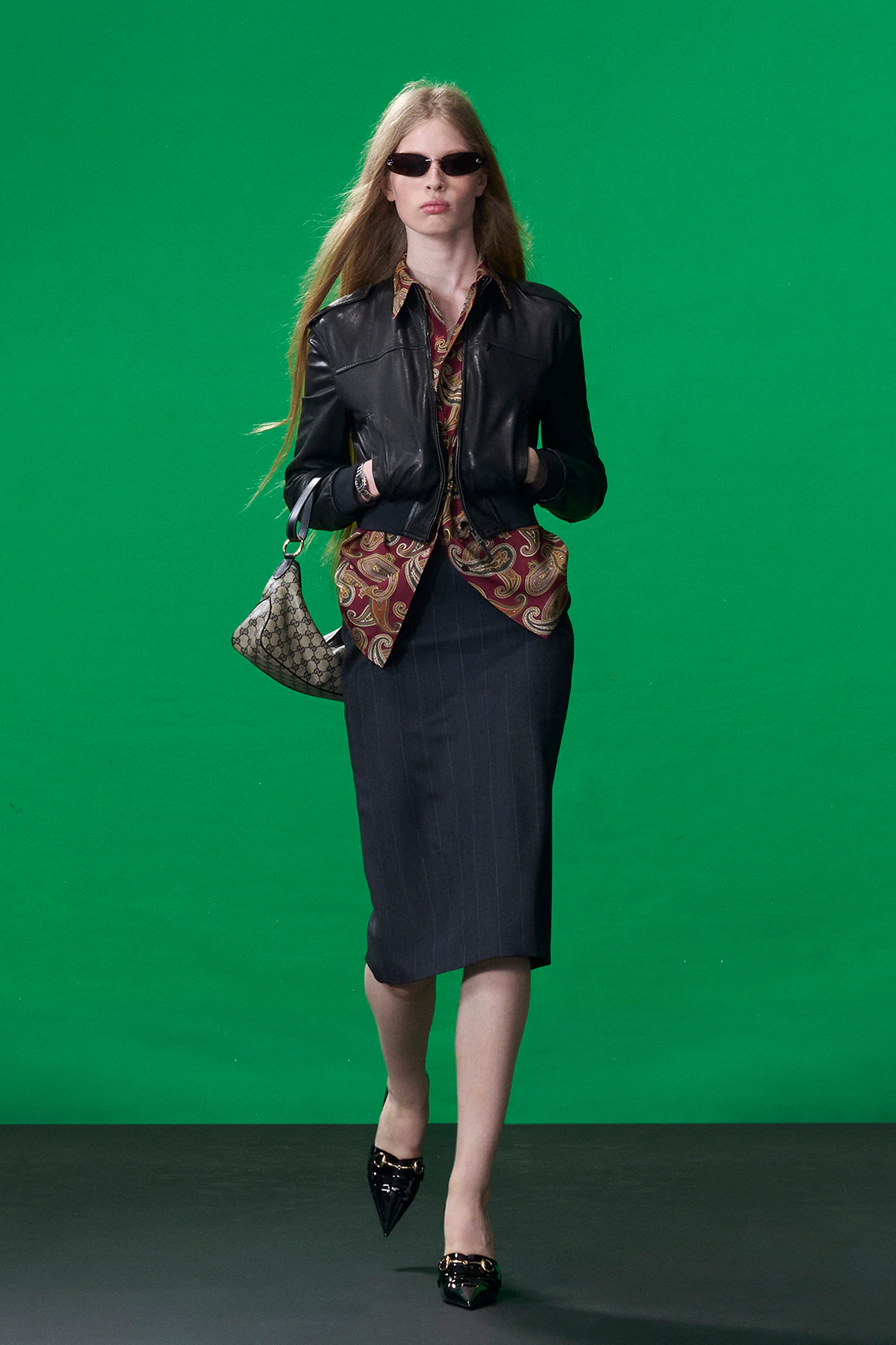 Model wearing black leather Gucci jacket with pencil skirt and paisley blouse during Gucci Resort 2027 runway