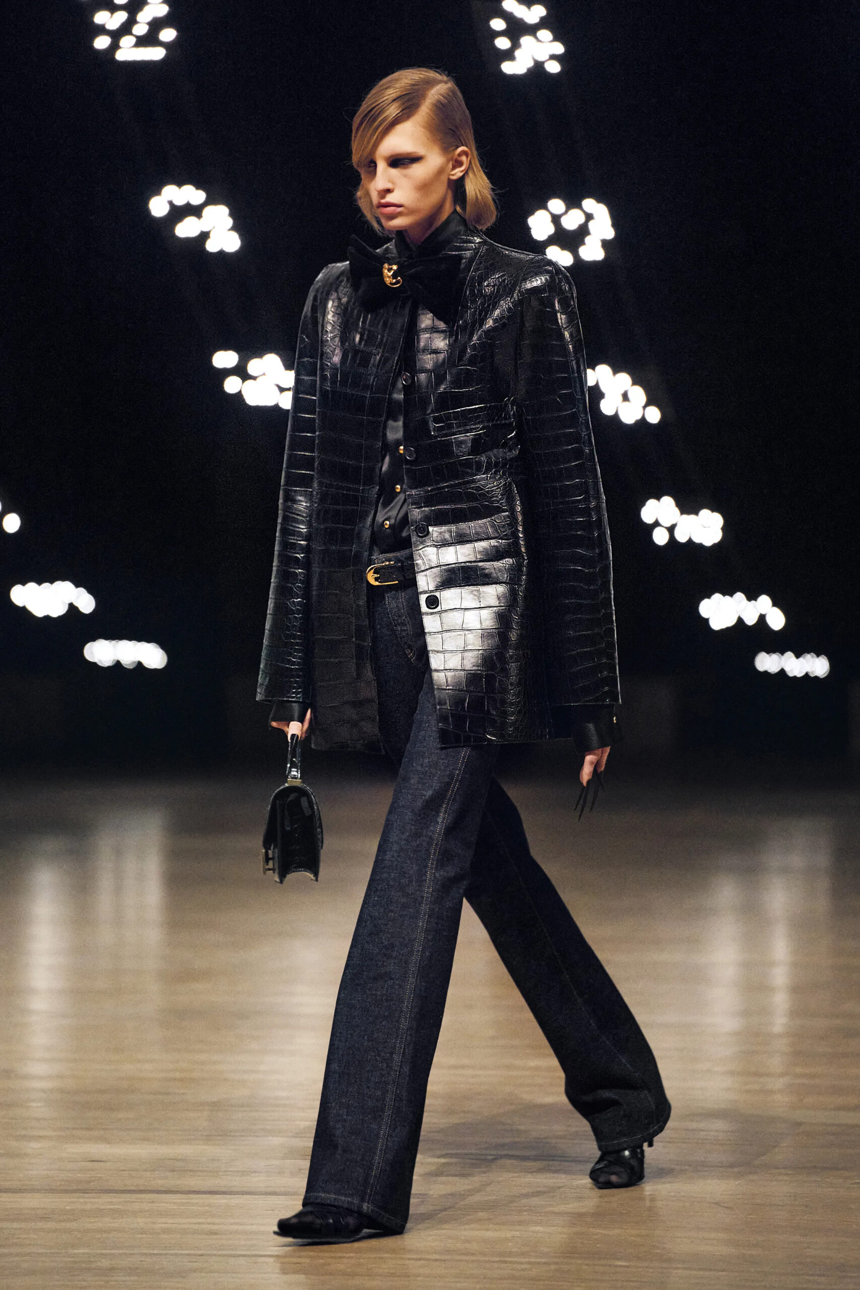 Model wearing a black crocodile-textured leather coat with dark denim at Khaite Fall Winter 2026 runway show