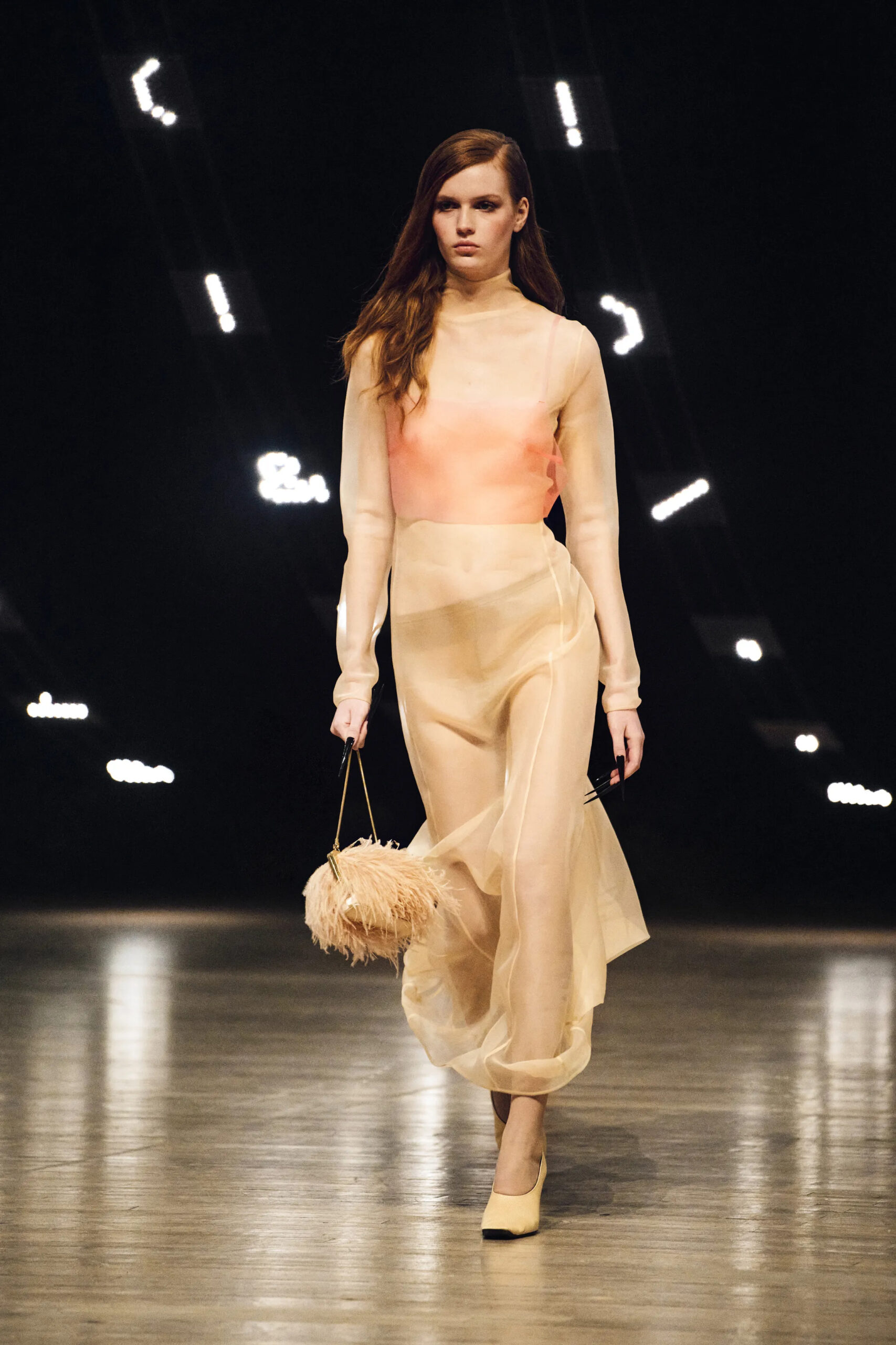 Model wearing a sheer blush-toned dress carrying a feathered handbag at Khaite Fall Winter 2026 runway show