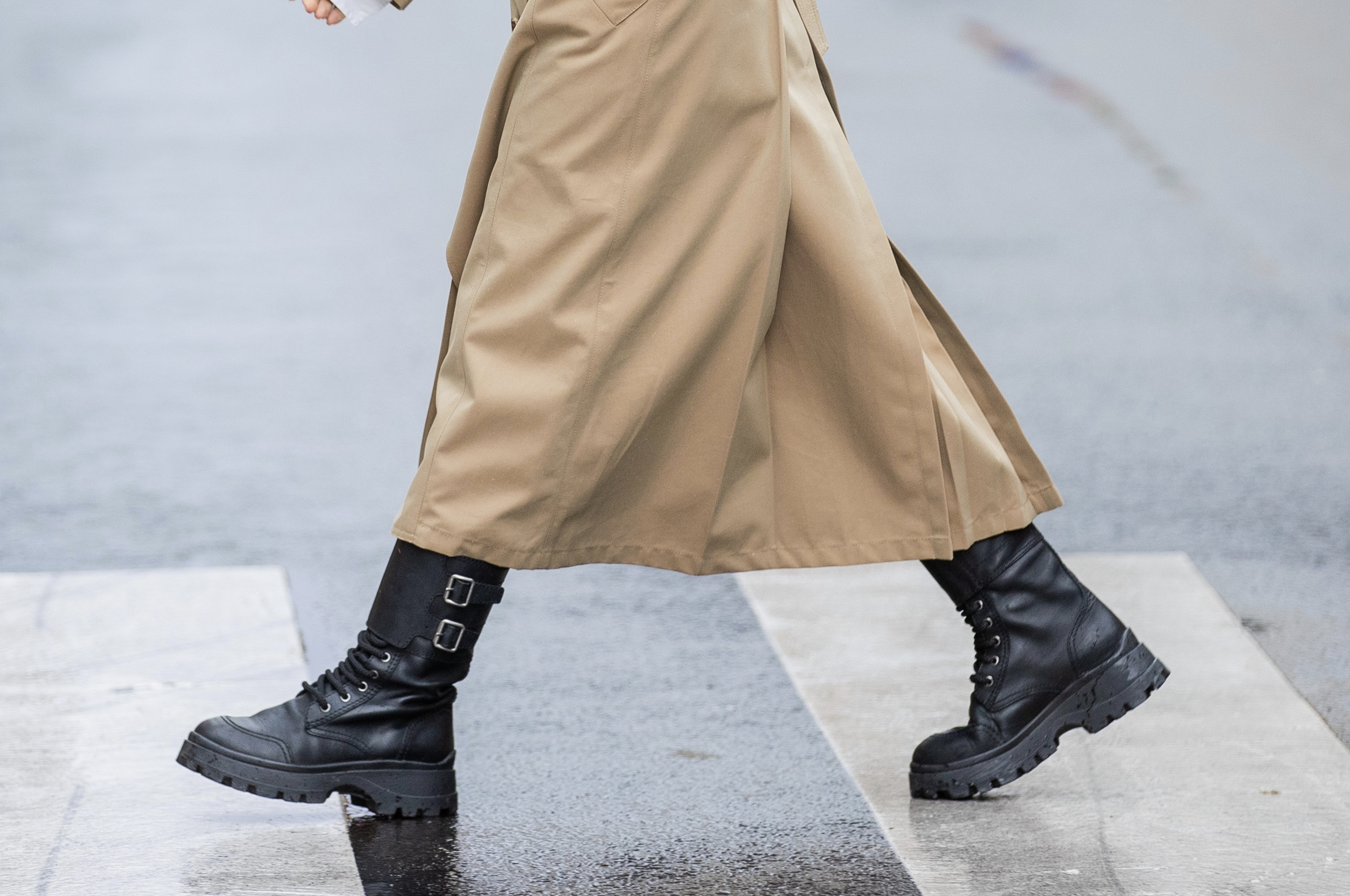Close-up detail of black combat boots crossing a Paris street on a rainy day during Fashion Week.