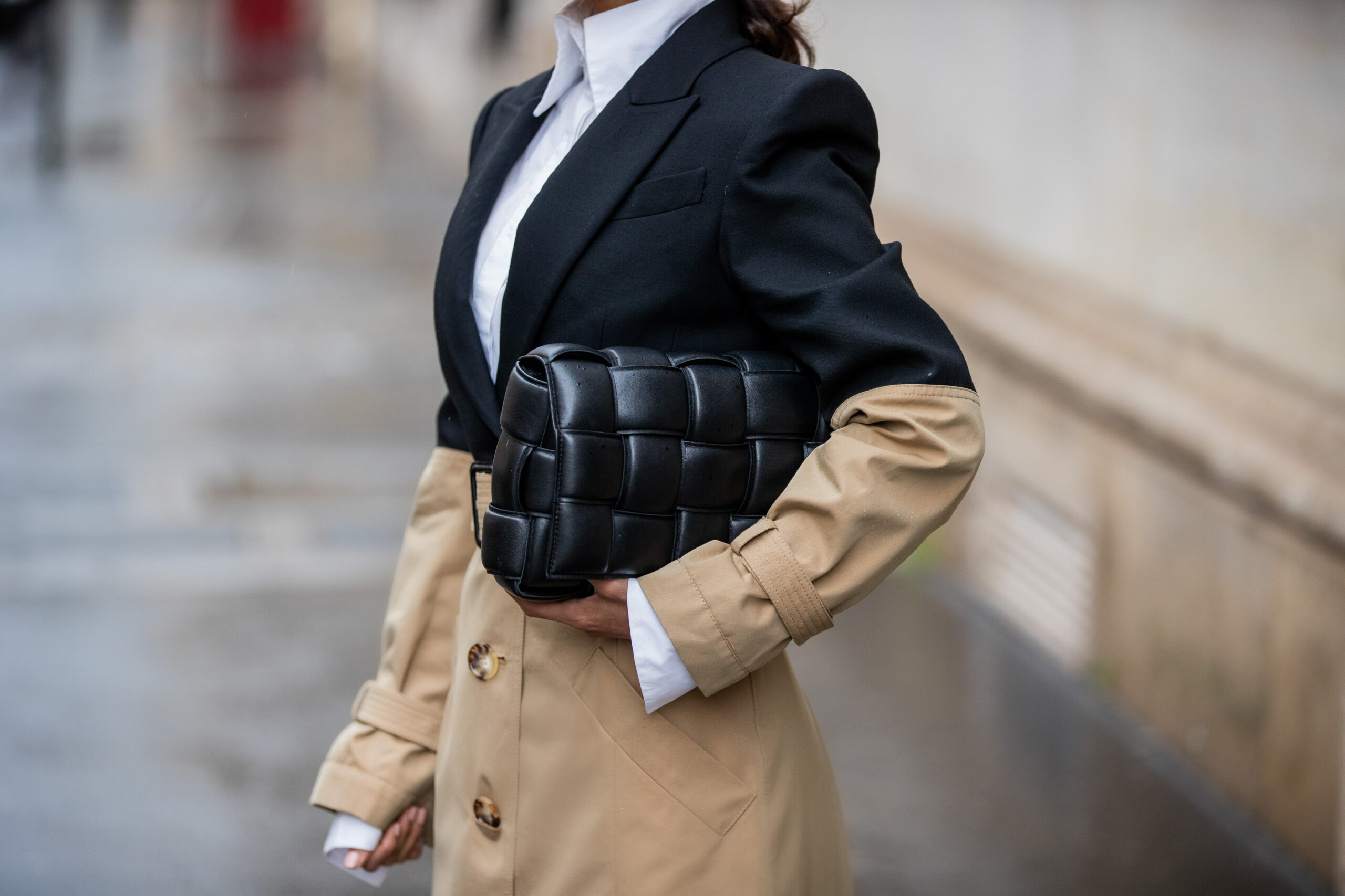 Close-up detail of a black woven leather clutch paired with a structured trench coat during Paris Fashion Week.