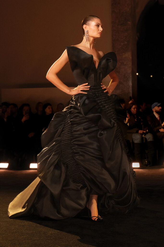 Model wearing a black sculptural Schiaparelli couture gown with exaggerated hips and dramatic folded neckline during Paris Haute Couture Week