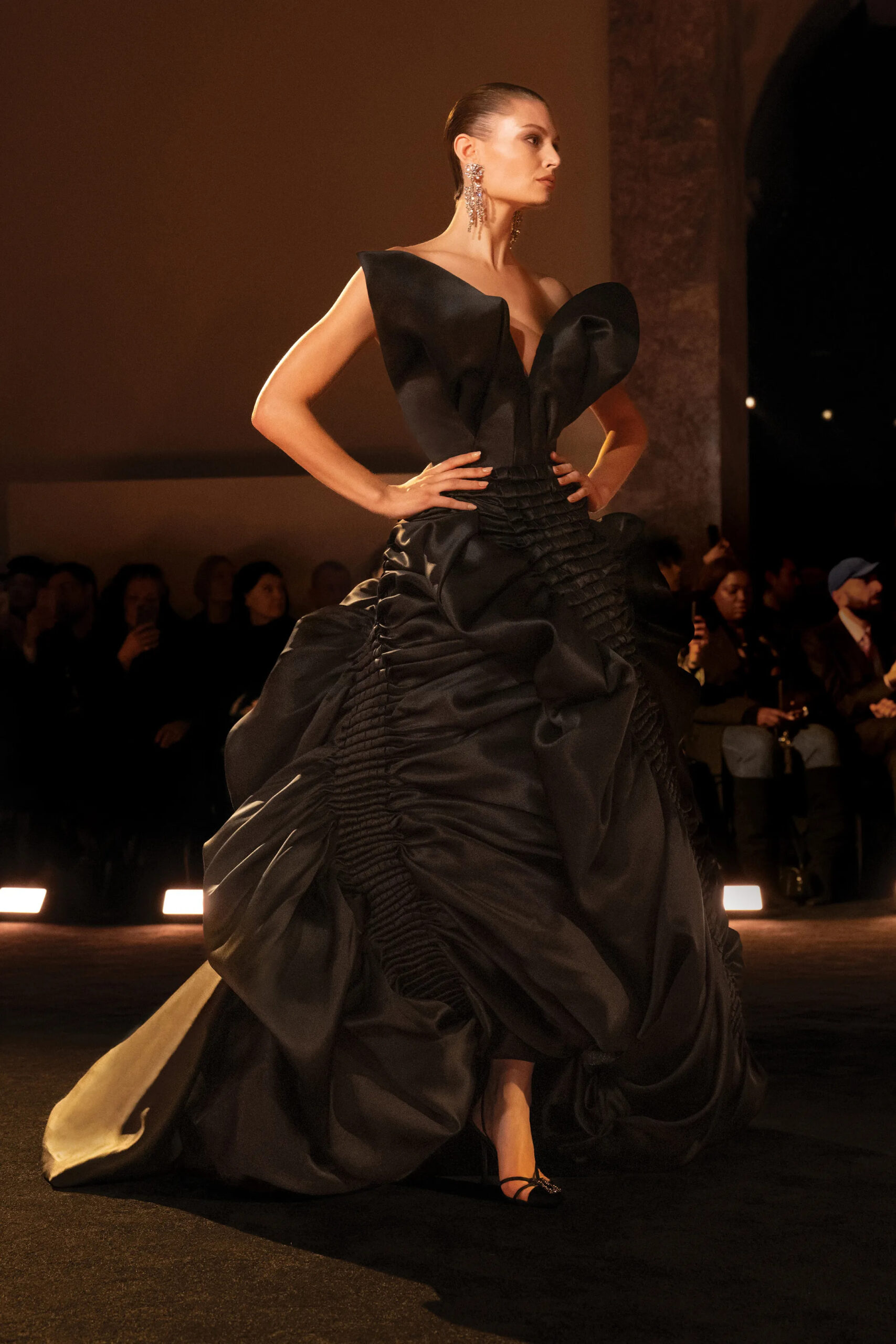 Model wearing a black sculptural Schiaparelli couture gown with exaggerated hips and dramatic folded neckline during Paris Haute Couture Week