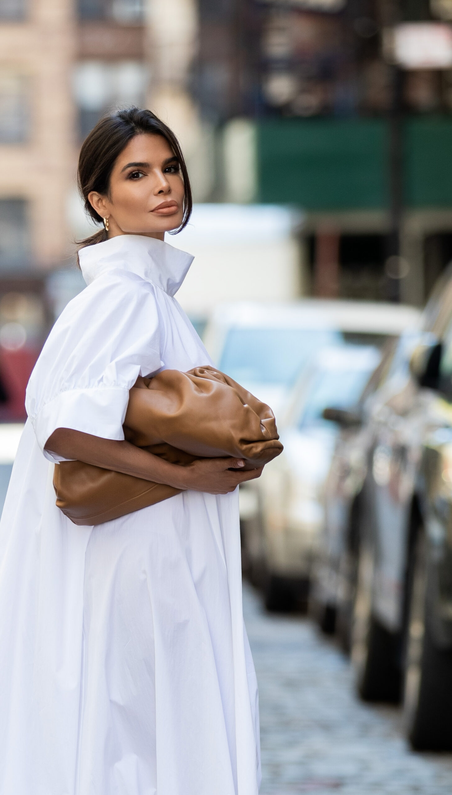 Portrait of Victoria Barbara wearing a white The Row dress with a dramatic collar and carrying a brown Bottega Veneta clutch.
