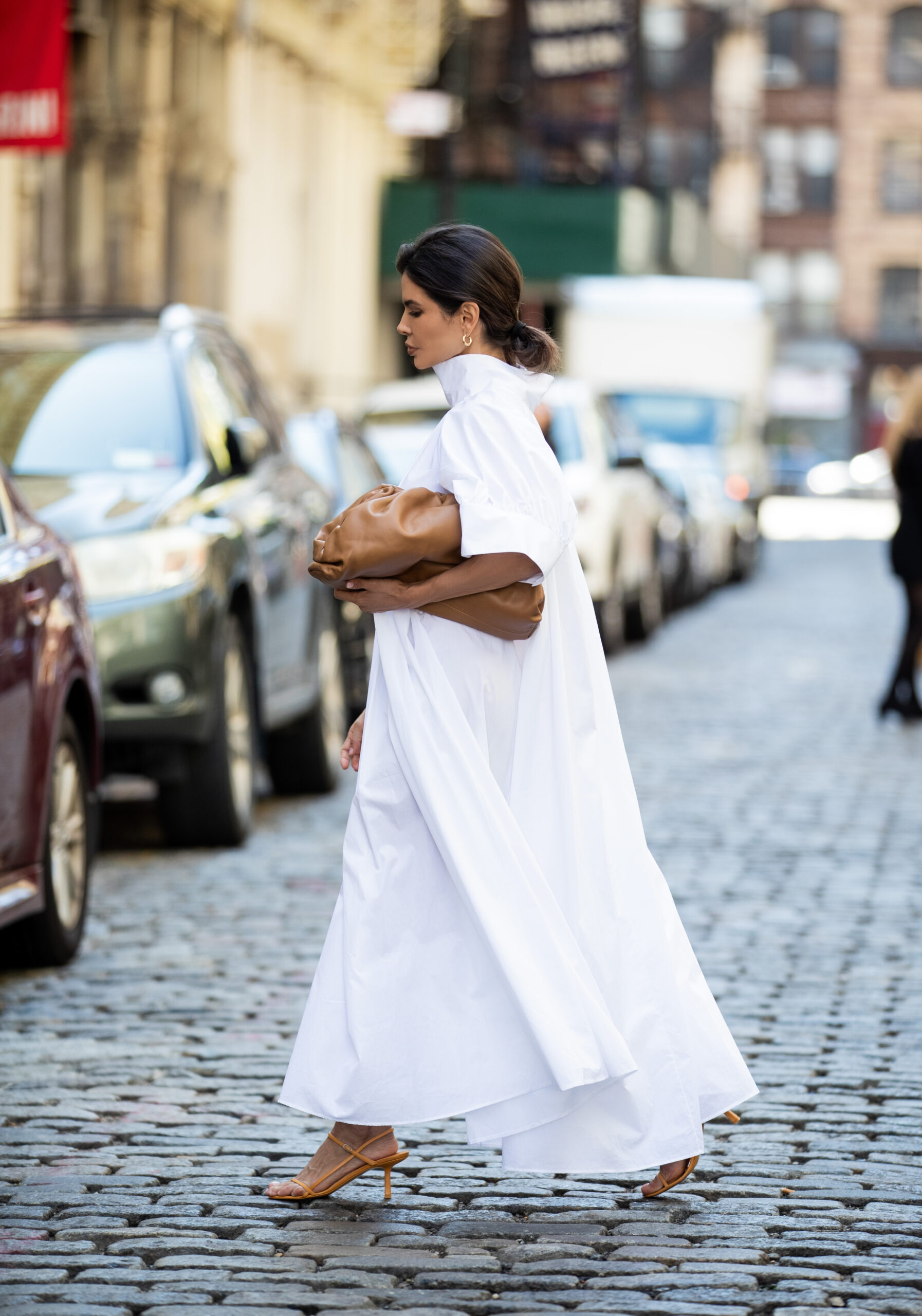 Side profile of Victoria Barbara walking through New York in a white The Row dress styled with The Row sandals and Bottega Veneta accessories.