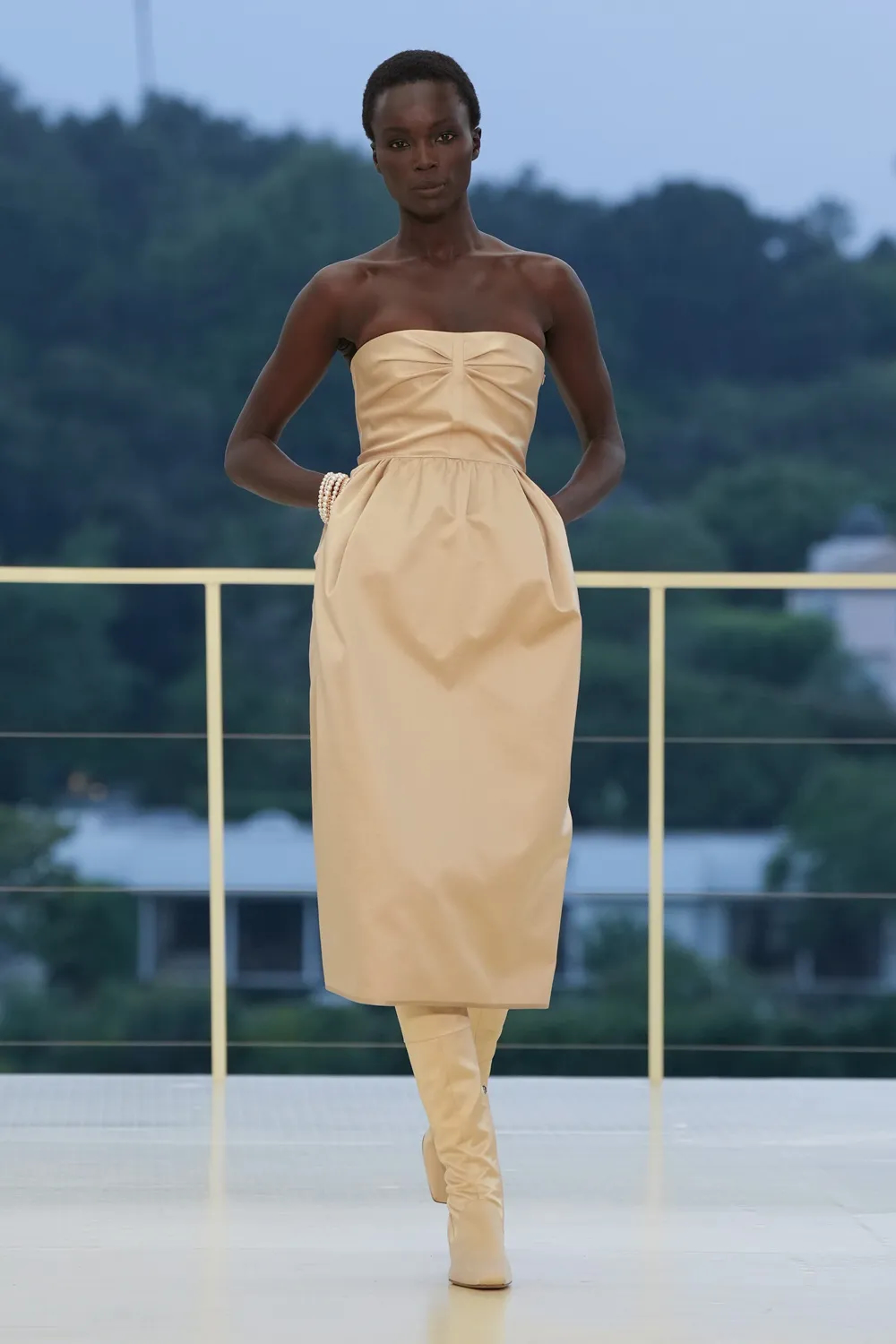 Model wearing an ivory strapless dress with gathered detailing and matching knee-high boots at the Hermès Fall-Winter 2026 runway presentation.