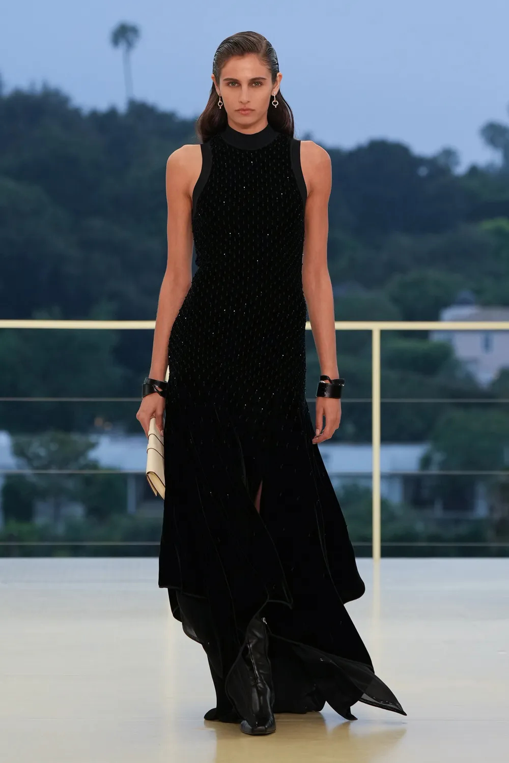 Model wearing a black sleeveless embellished evening gown with a high neckline, leather cuffs, and boots at the Hermès Fall-Winter 2026 runway show.