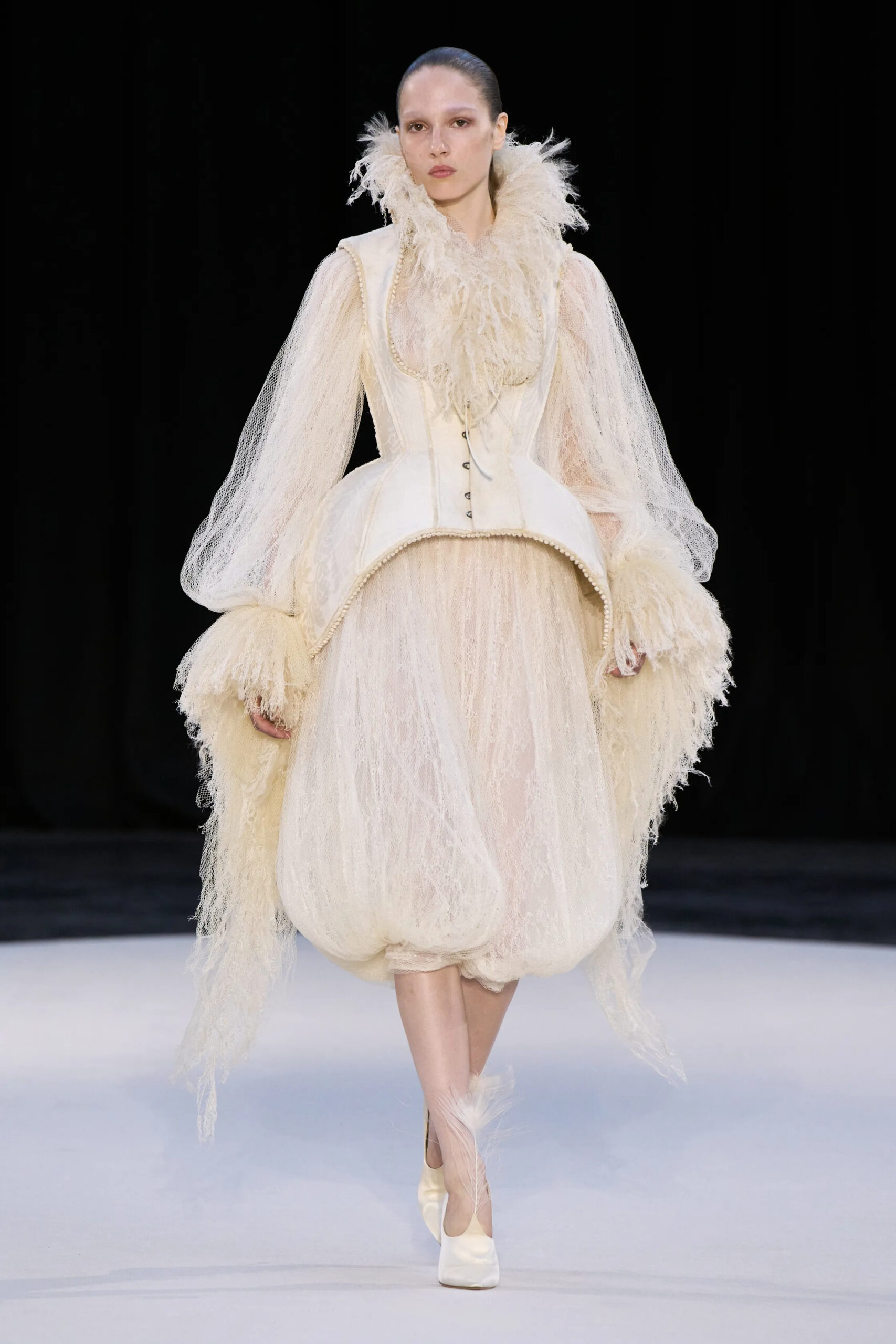 Model wearing an ivory corseted couture look with exaggerated rounded volume and feathered details by Ashi Studio Fall 2026 Couture