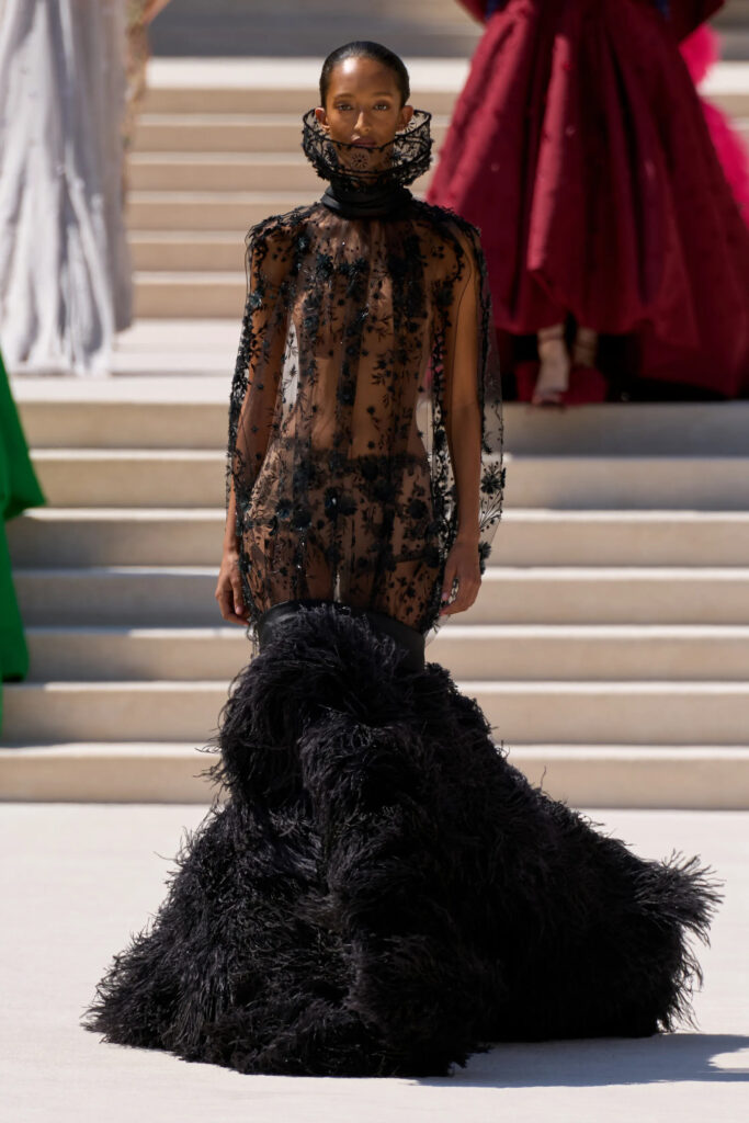 Model wearing a sheer black lace couture gown with a dramatic feathered skirt by Balenciaga