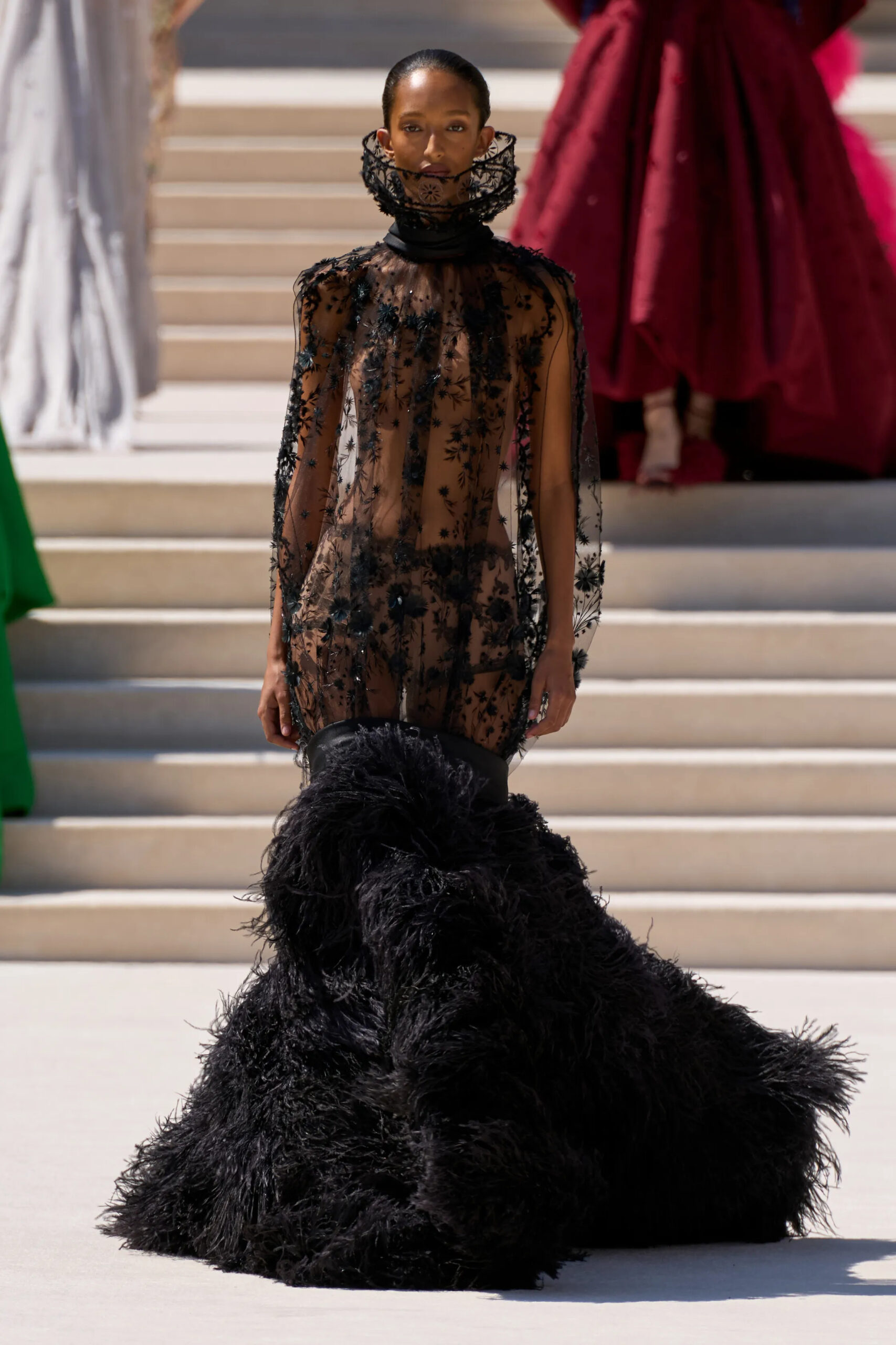 Model wearing a sheer black lace couture gown with a dramatic feathered skirt by Balenciaga