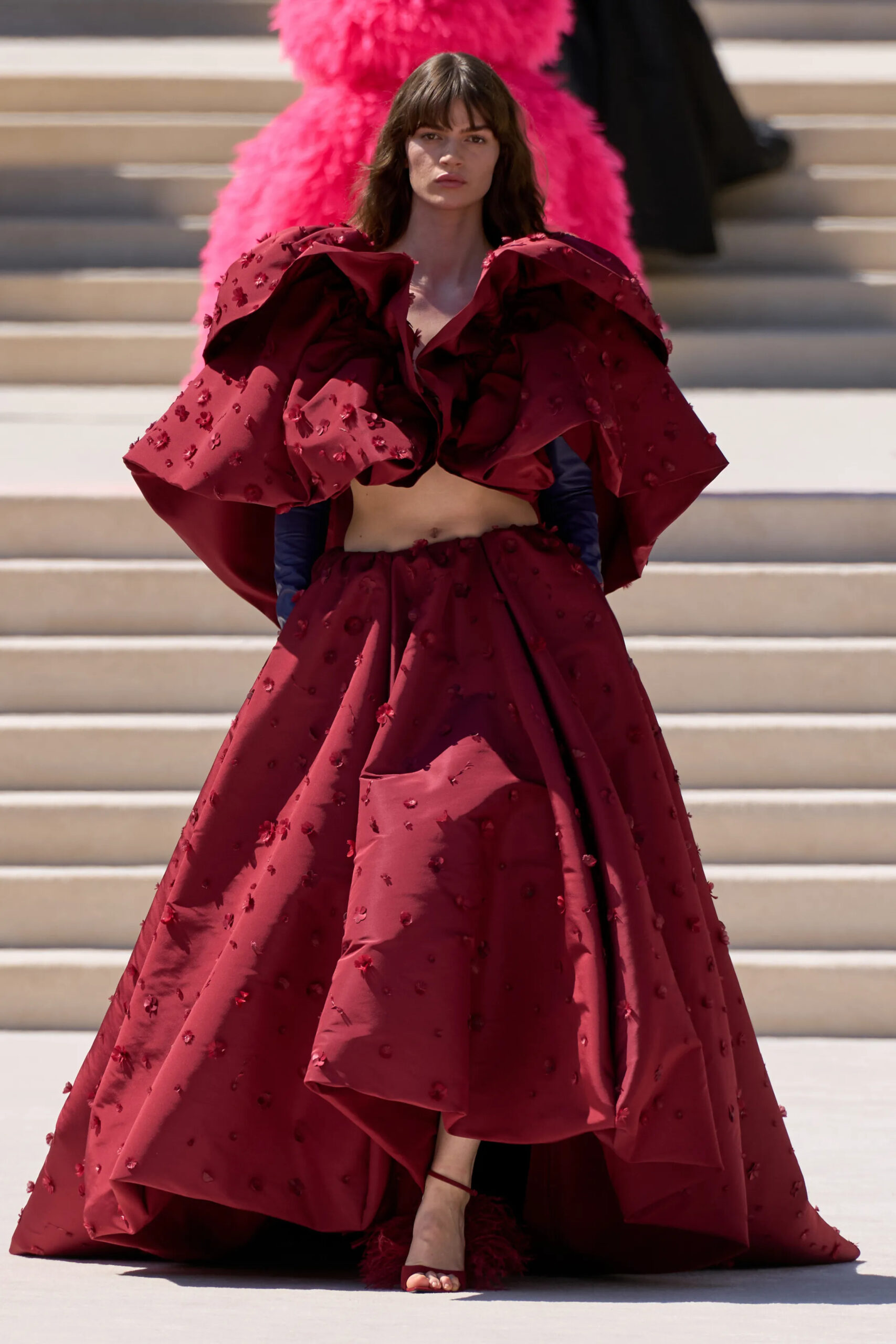 Model wearing a sculptural crimson Balenciaga Fall 2026 Couture gown featuring dramatic architectural volume, hand embellishments, and an exaggerated overskirt by Pierpaolo Piccioli