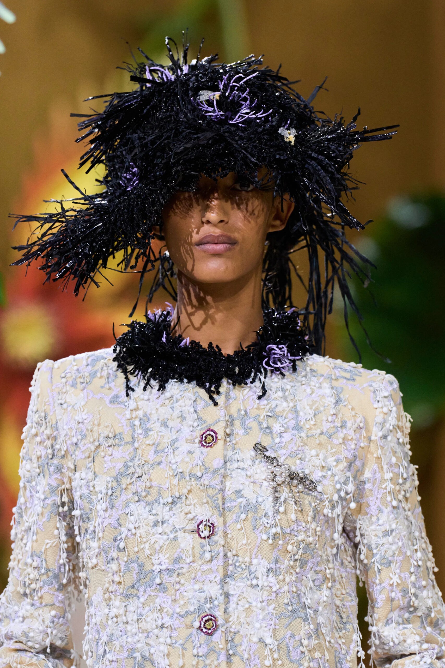 Close-up of a white embroidered Chanel couture jacket paired with a dramatic black feathered hat