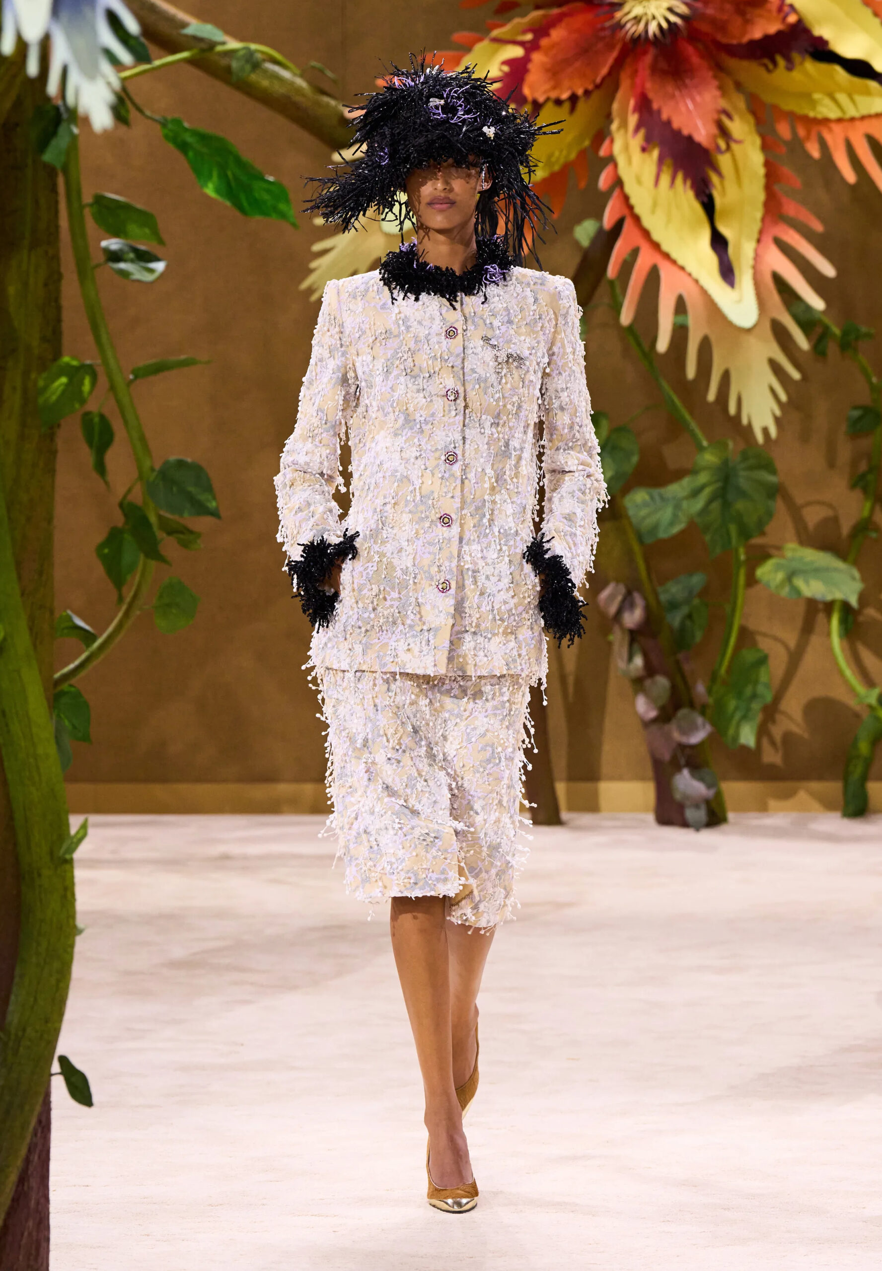 Model wearing a white textured Chanel couture skirt suit with black feathered trim and an oversized feathered hat
