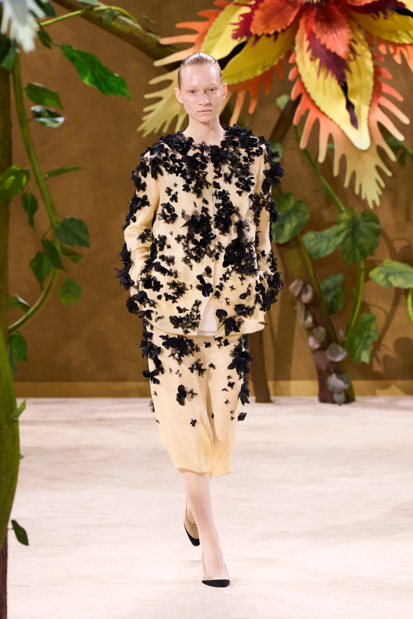 Model wearing a cream Chanel couture dress covered with black floral appliqué embellishments