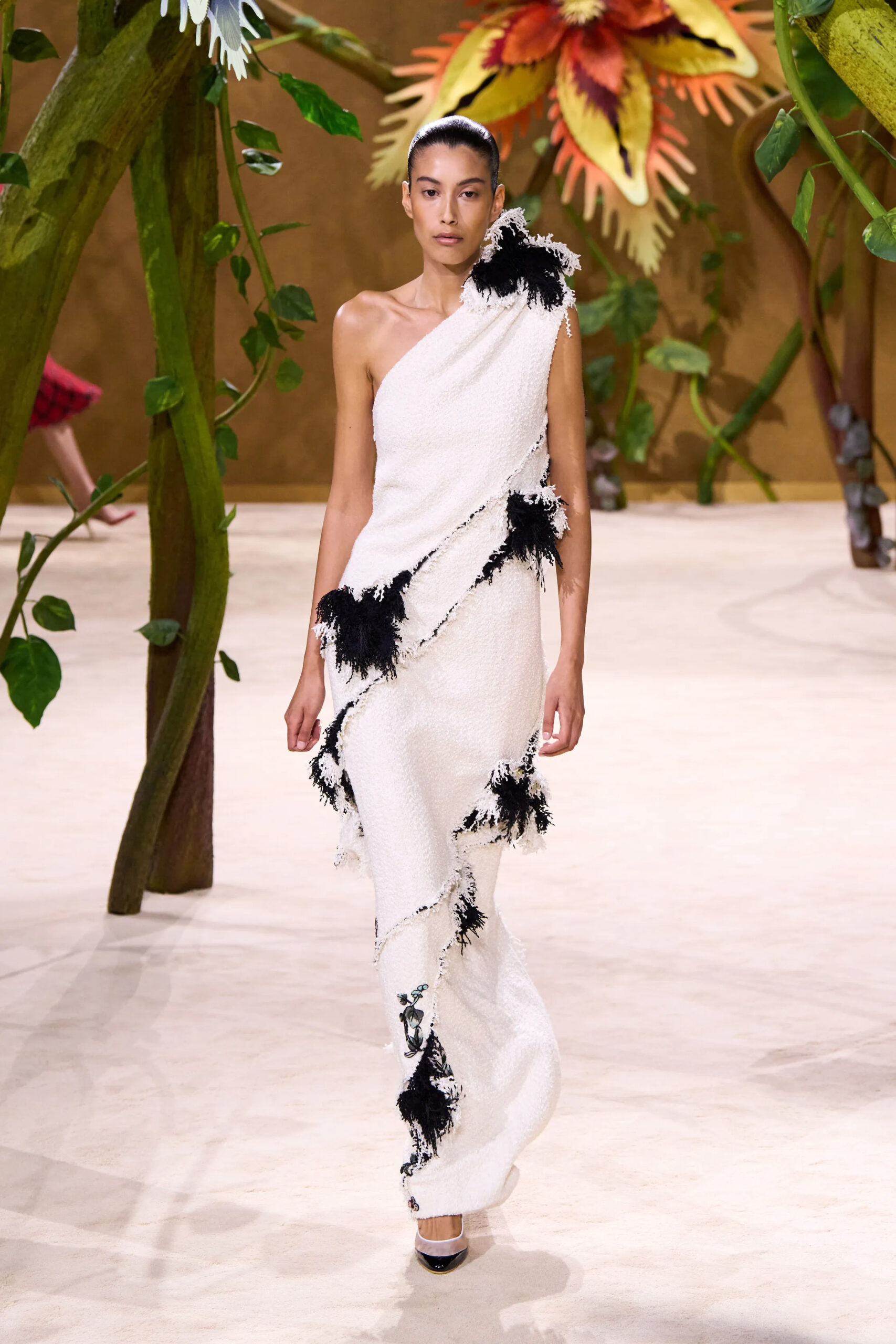 Model wearing a white one-shoulder Chanel couture gown accented with black feather embellishments