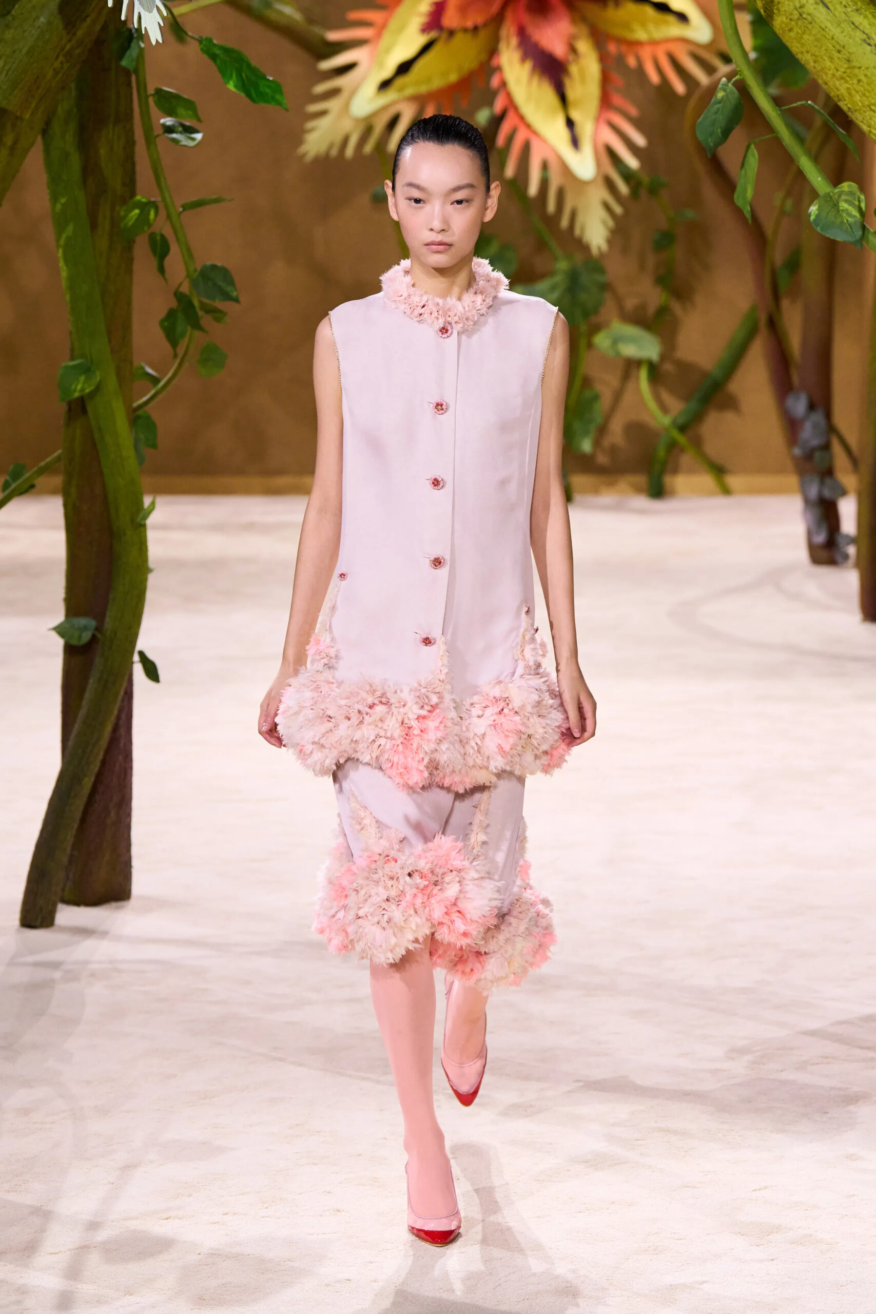Model wearing an ivory Chanel couture ensemble with blush feather trim at the neckline, hem, and trousers