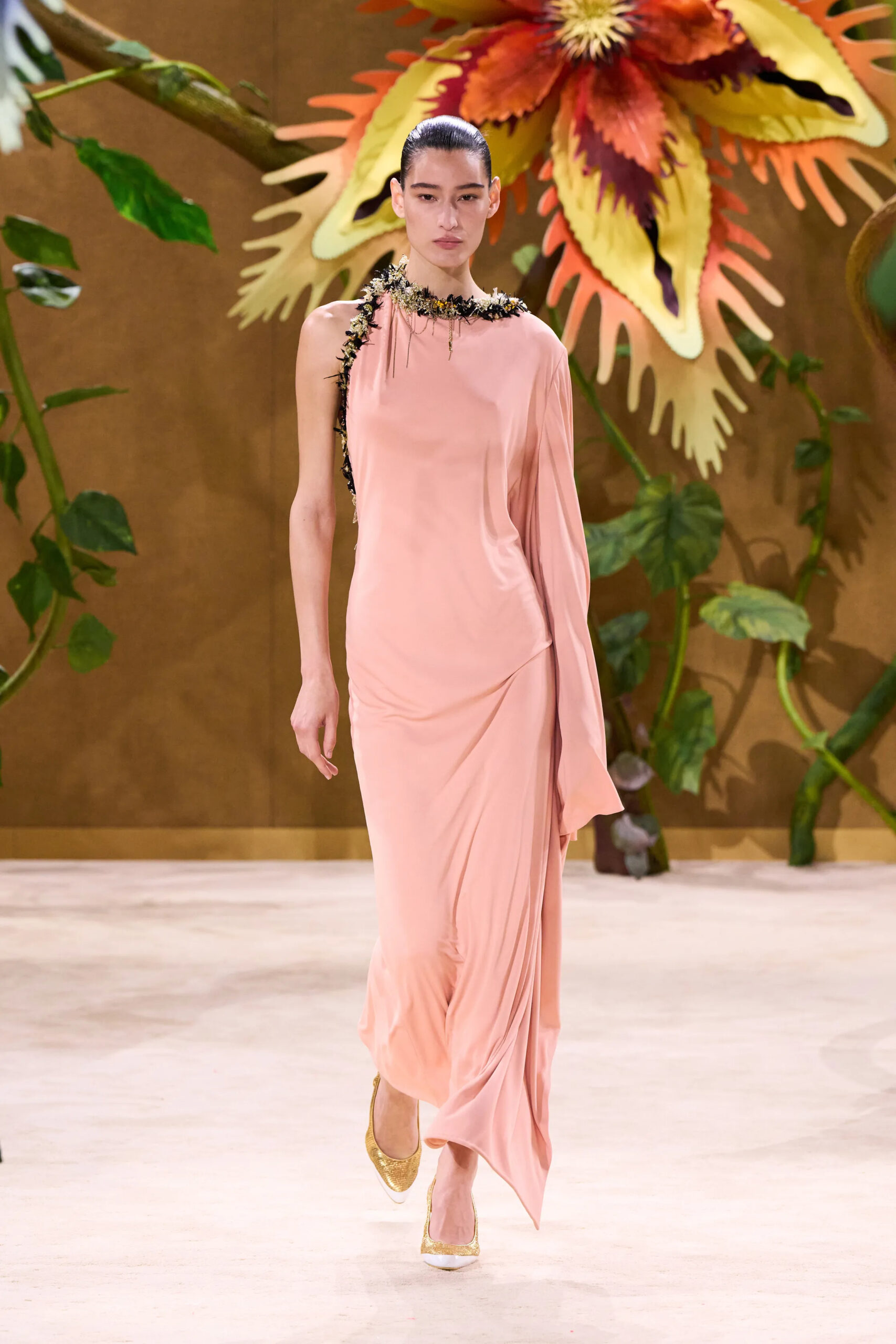 Model wearing a blush pink asymmetrical Chanel couture gown with delicate embellishment around the neckline