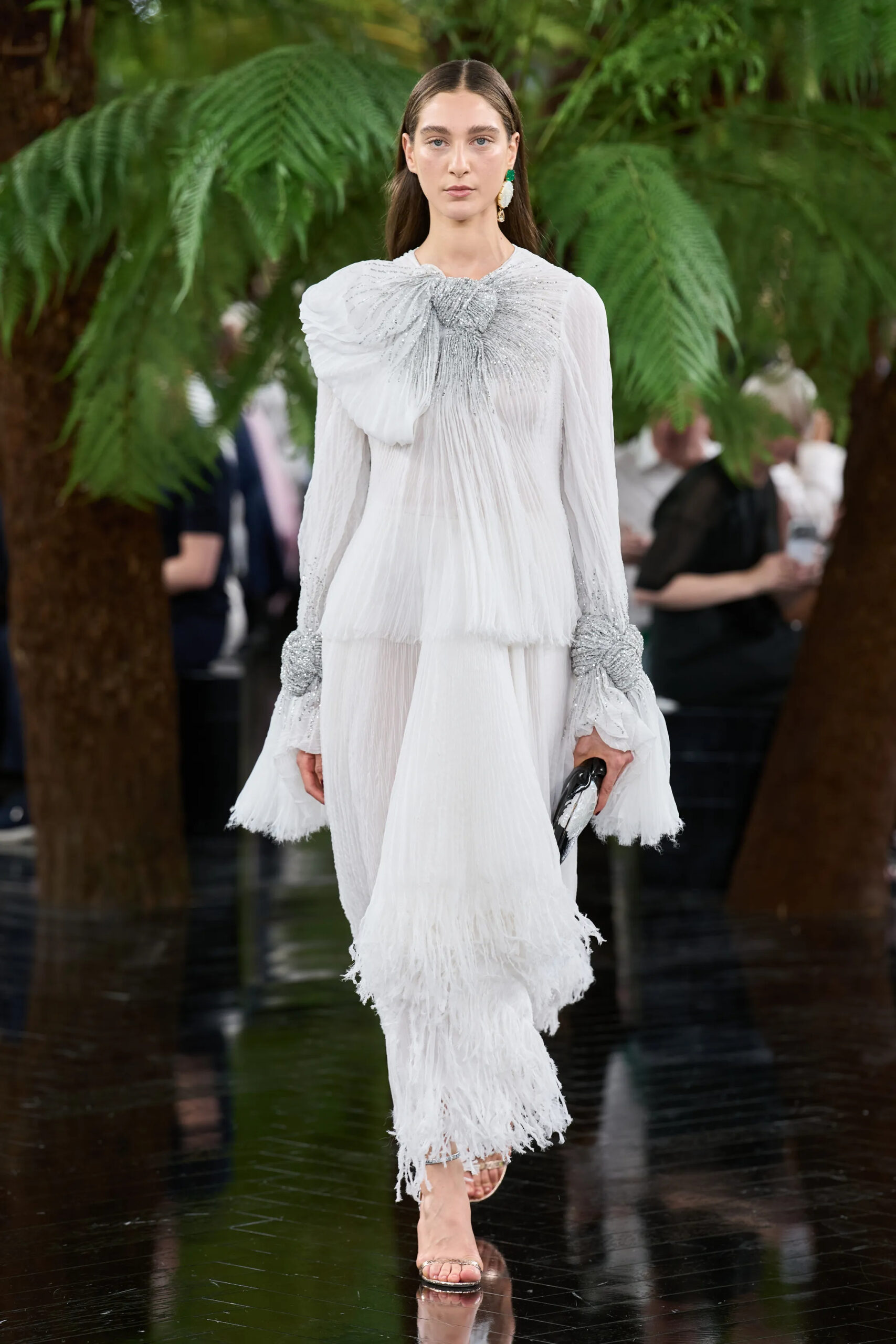 Model wearing a white pleated Dior Fall 2026 Couture dress with sculptural shoulder detailing and flowing fringe
