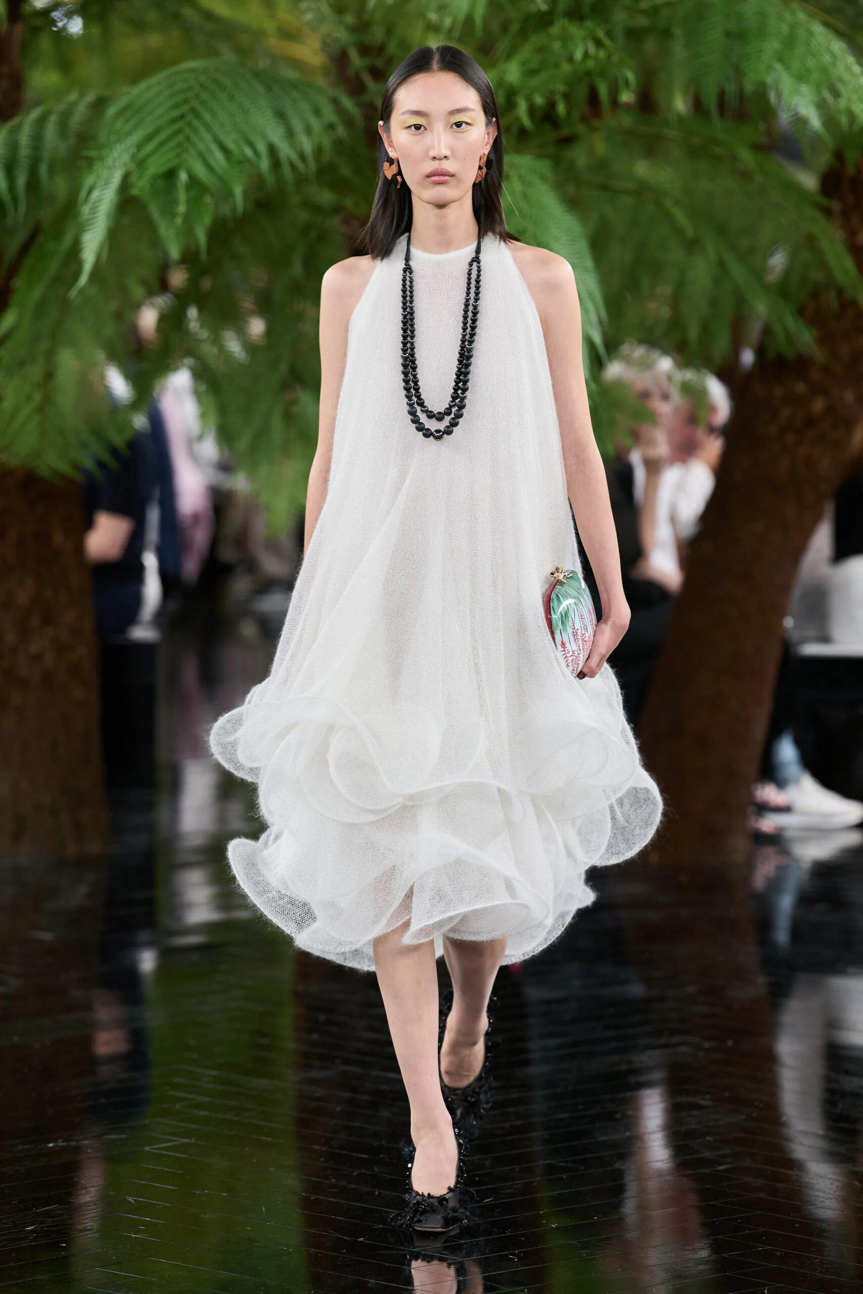 Model wearing a sleeveless white Dior Fall 2026 Couture dress with layered volume and botanical-inspired minaudière