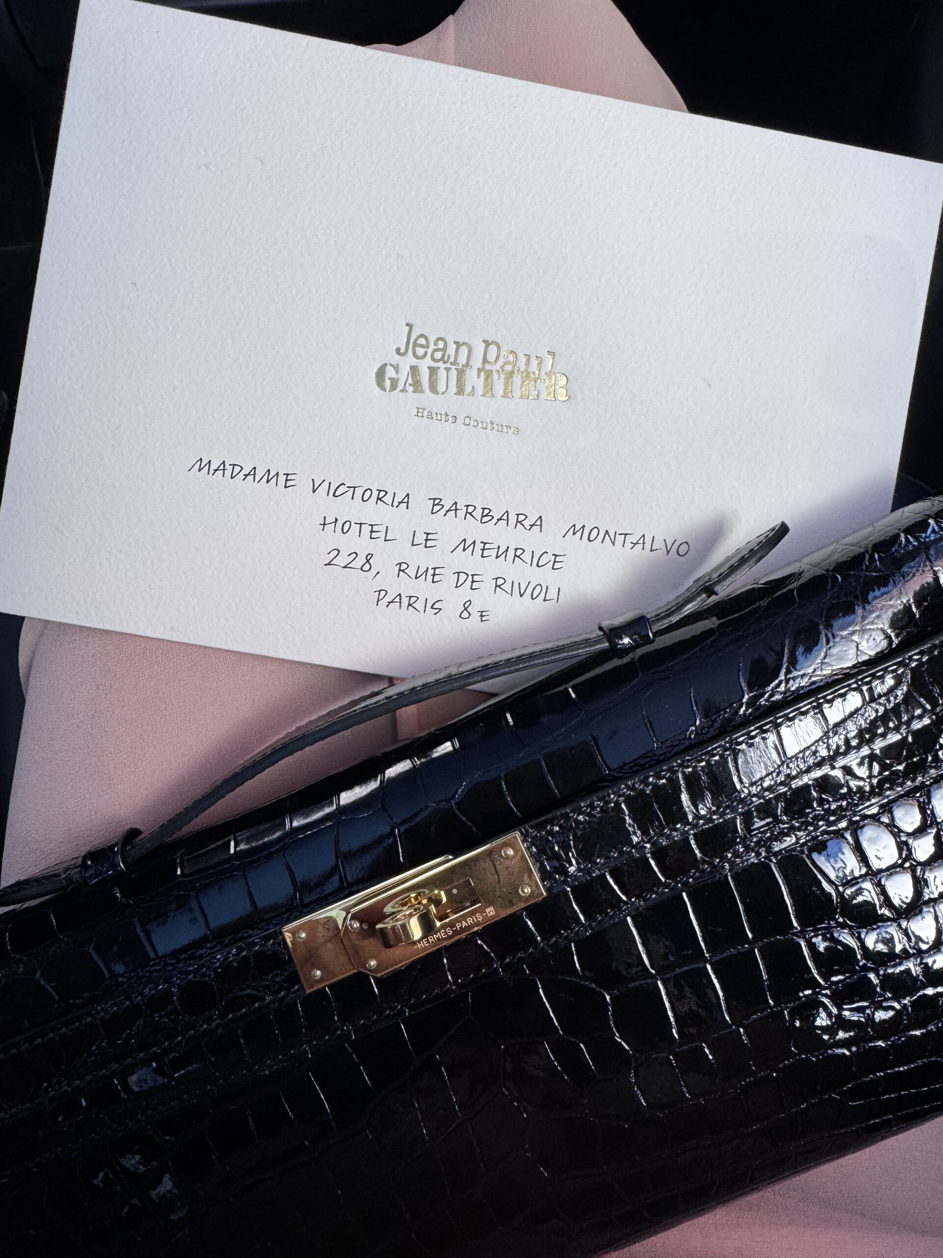 Official invitation to the Jean Paul Gaultier Fall/Winter 2026–2027 Haute Couture runway show beside a Hermès Kelly handbag